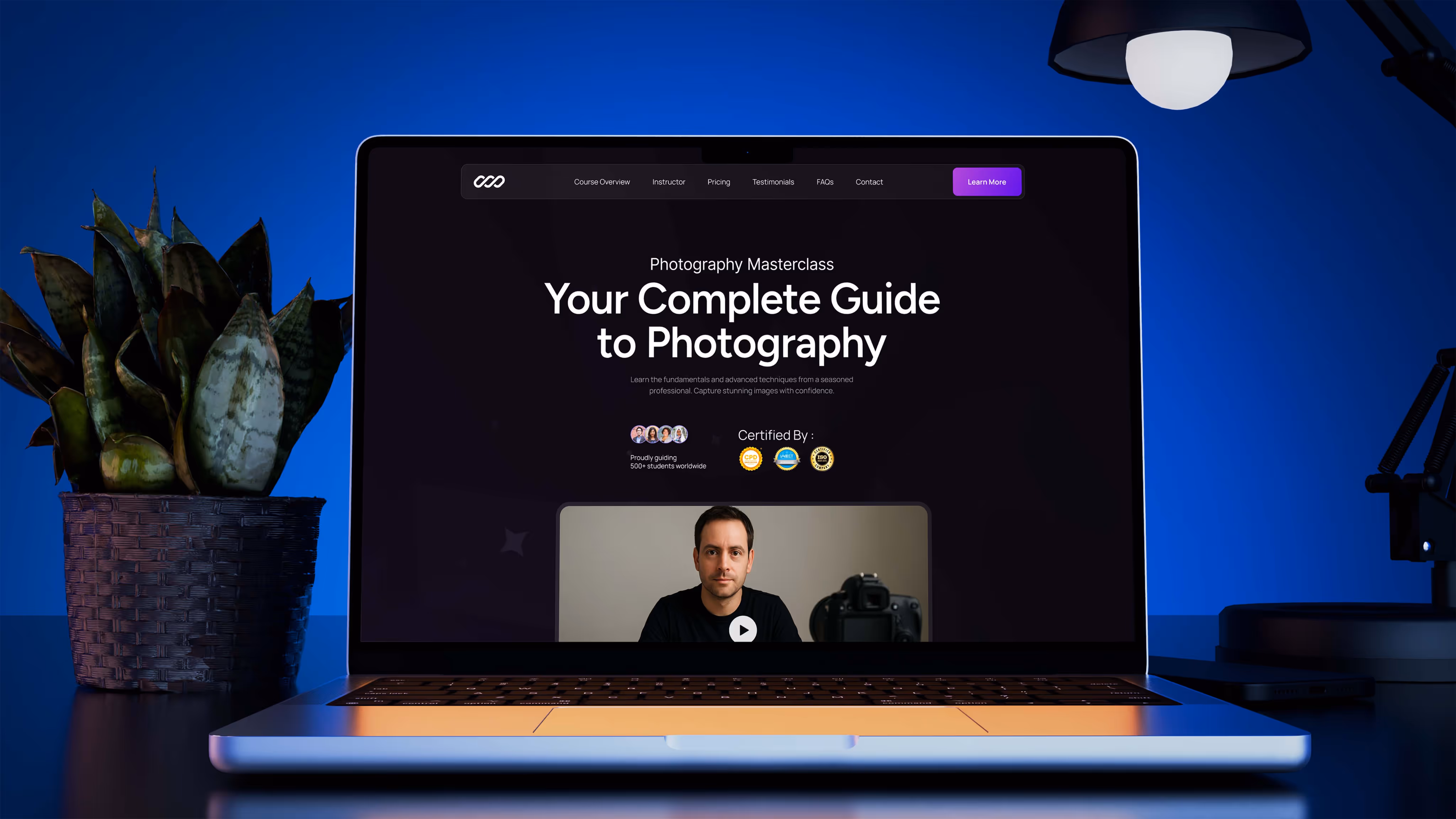 Laptop displaying a photography masterclass homepage with dark theme UI, set in a moody blue-lit workspace with plant decor and desk lamp.