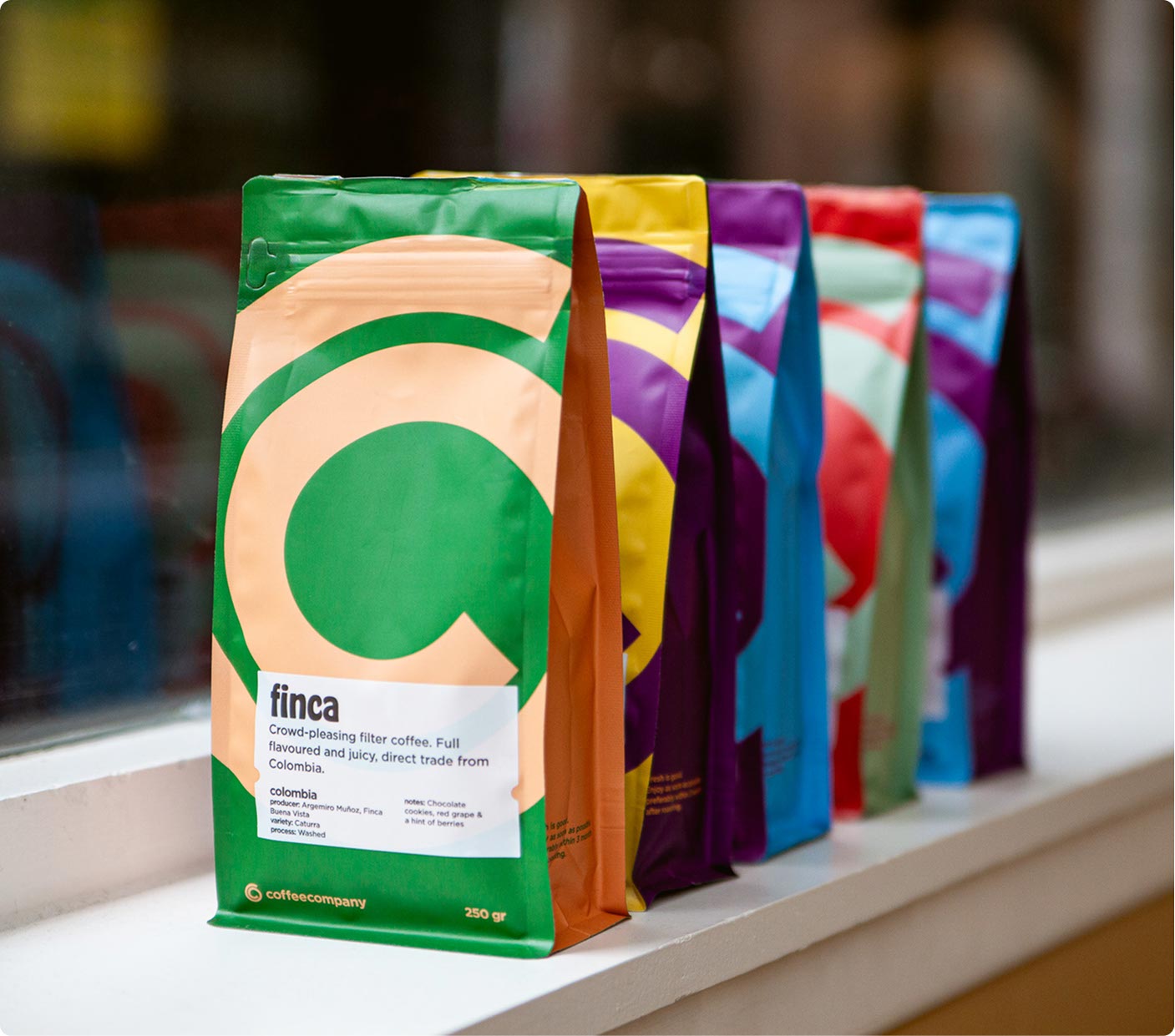 Row of colorful Coffeecompany coffee bags lined up on a windowsill.