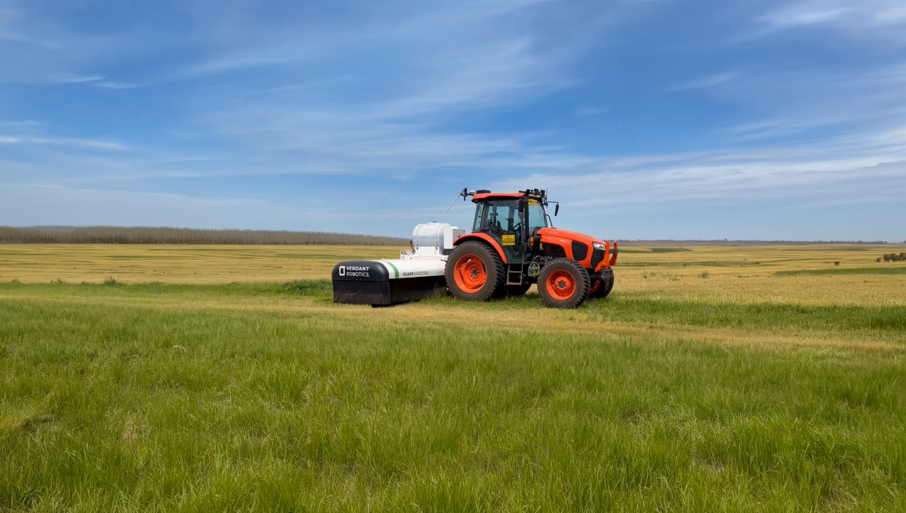 Red tractor attached to Verdant Robotics Sharp Shooter machine in a vast green and yellow field under blue sky.