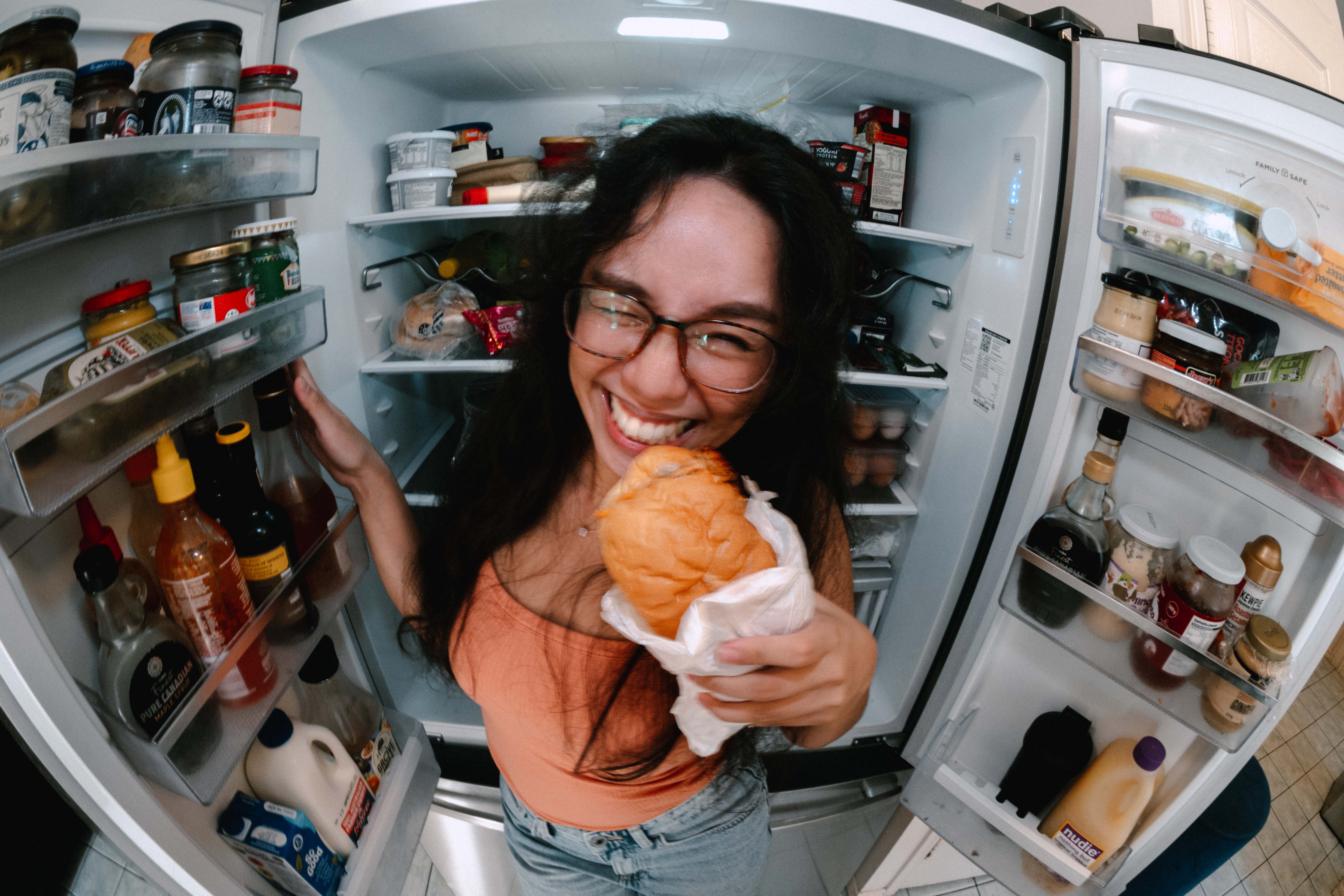 Angled shot of a smiling woman with glasses, holding a tray of sushi in one hand and chopsticks in the other
