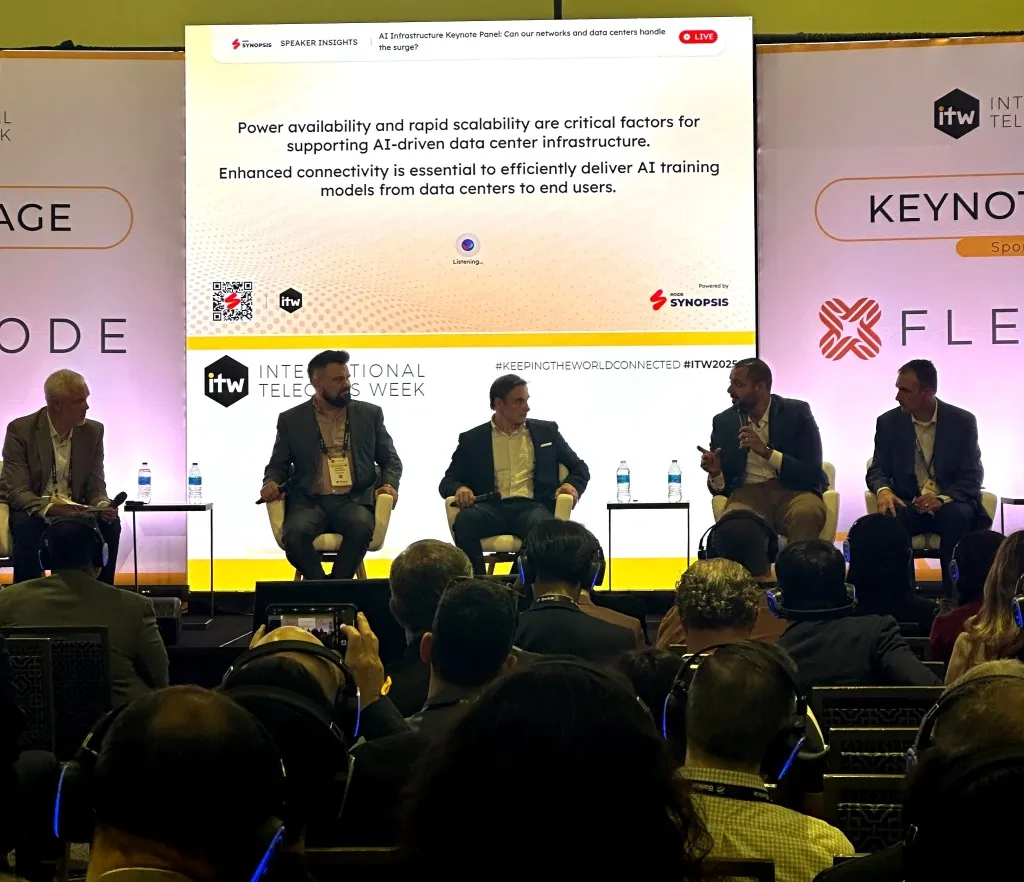 Audience seated and watching a speaker on stage in a dimly lit conference hall.
