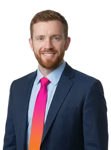 Smiling man with red hair and beard wearing a navy suit and pink tie.