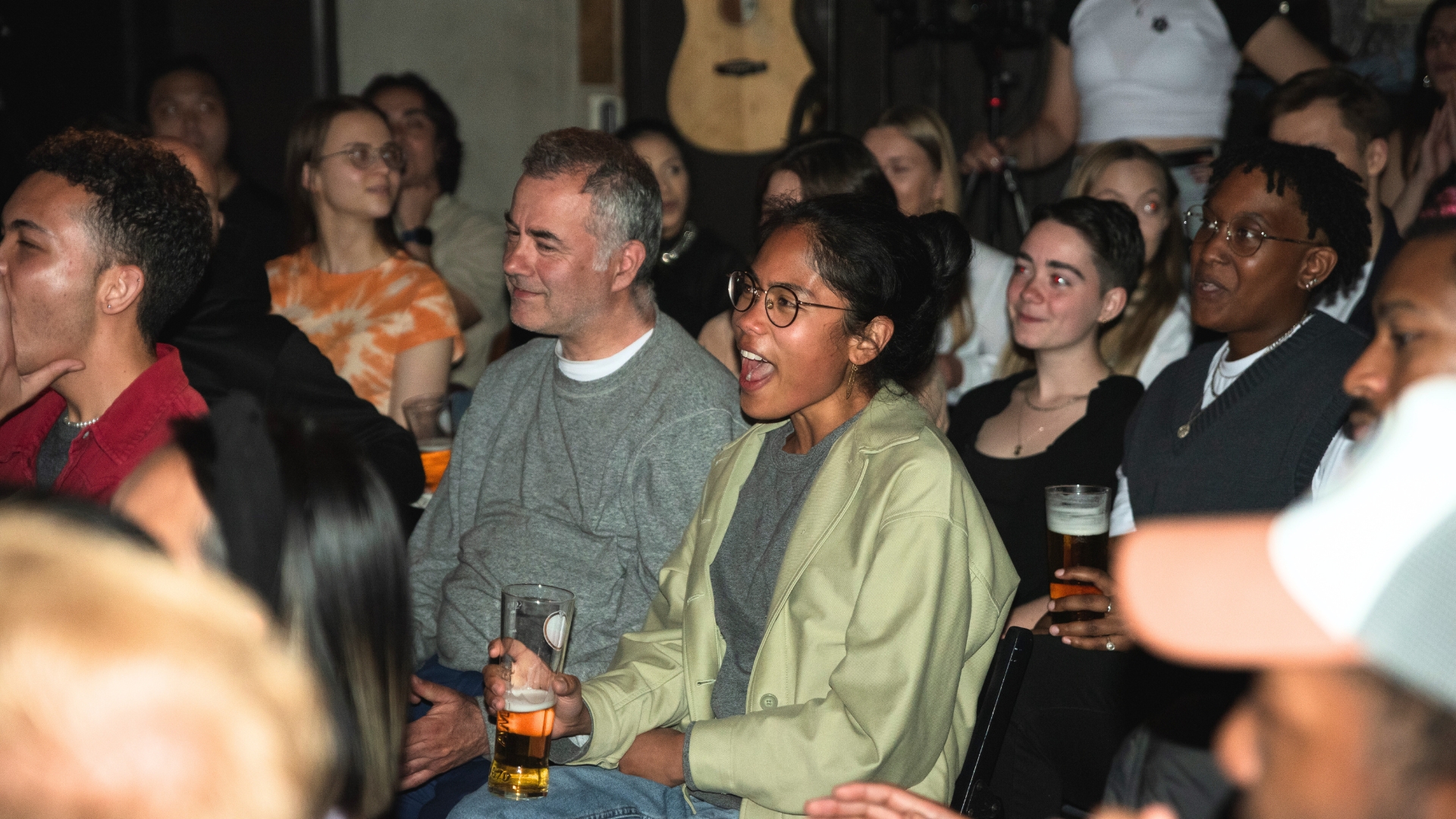 A diverse group of audience members with smiling faces, some holding drinks, attentively watching a comedian on stage in at Comedy Freaks, highlighting the engaging and unique experience of London comedy shows.
