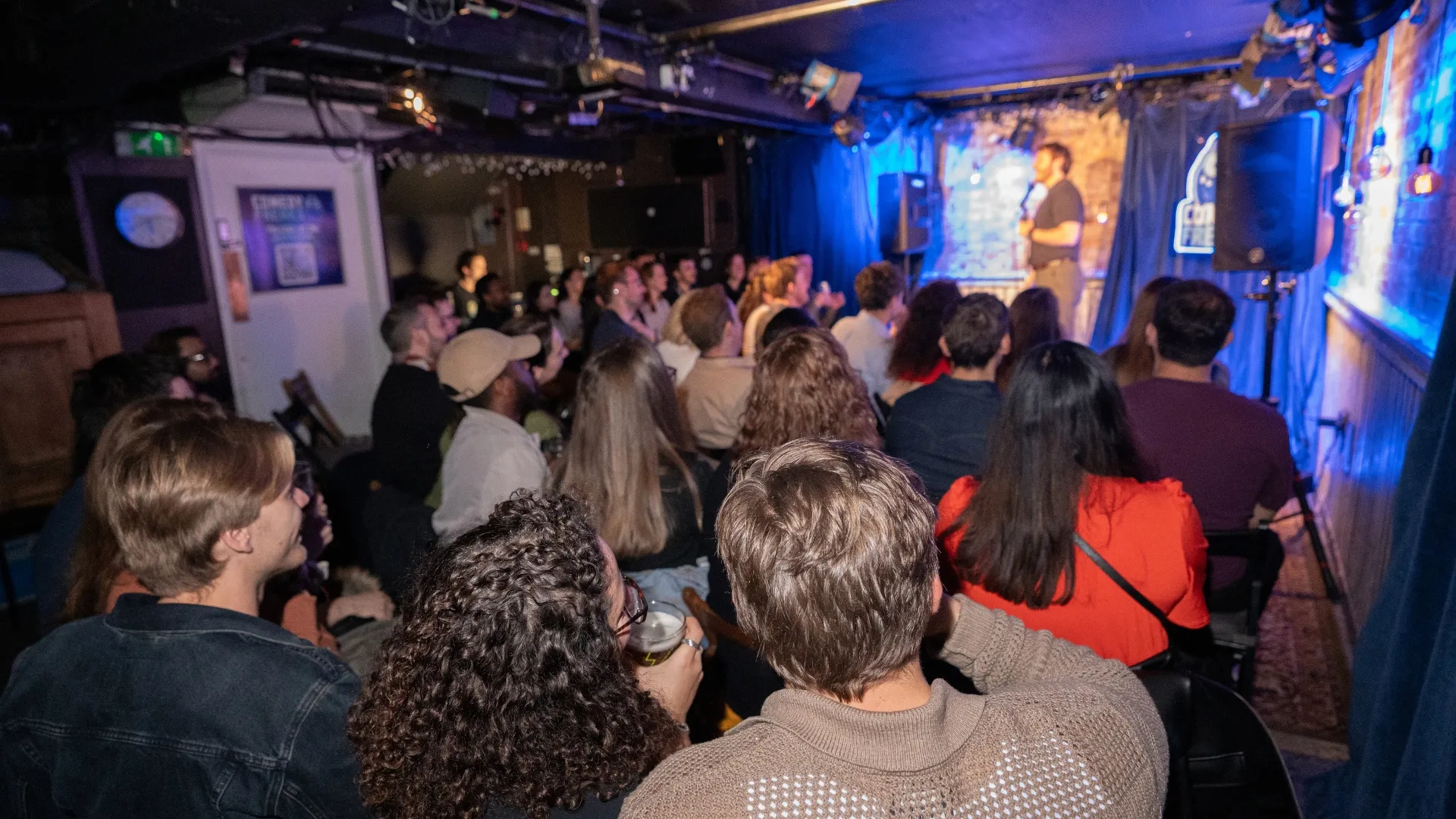 A wide shot of a packed and lively audience enjoying a live comedy show at Comedy Freaks, showcasing the raucous, energetic, and fun atmosphere that feels like the best house party , at the wildest comedy club in London.