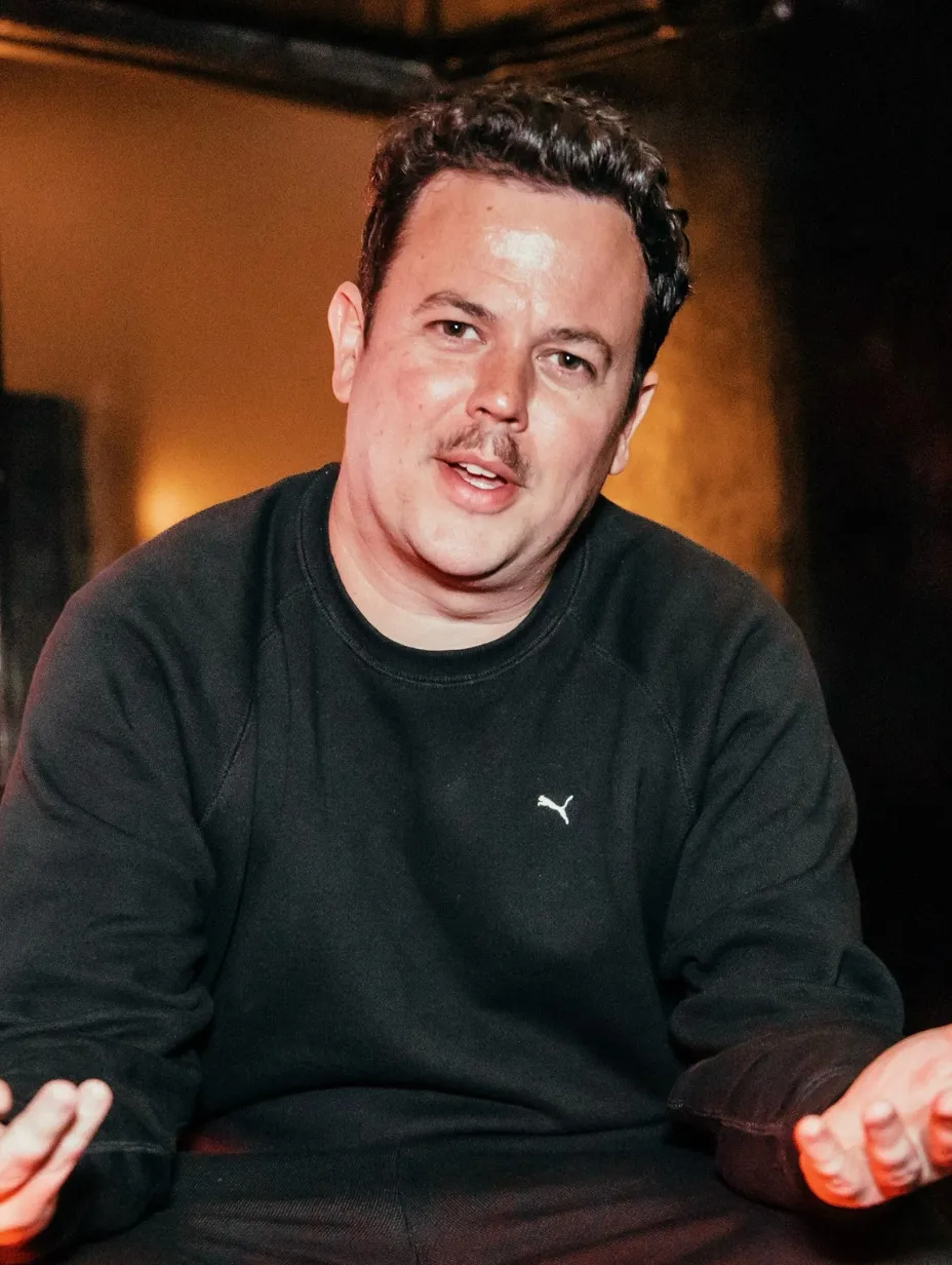 Michael Turner, a male comedian with dark hair and a moustache, looks towards the camera with a slight smile, wearing a black sweatshirt. He's ready to deliver engaging stand-up comedy at a Comedy Freaks comedy show London