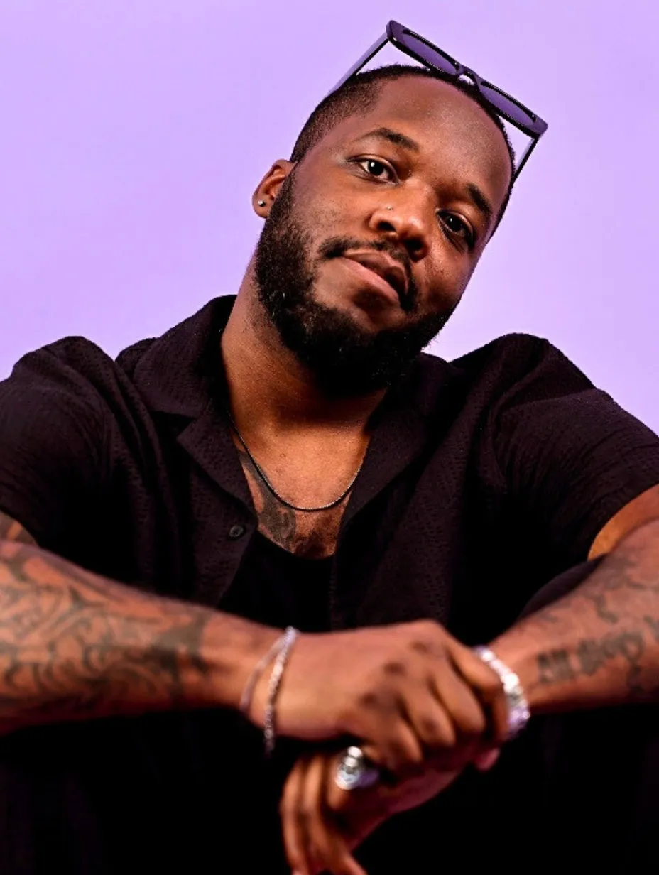 Tevin Everett, a male comedian with a beard and sunglasses on his head, looks confidently at the camera, wearing a dark shirt and showcasing tattoos on his arms, embodying the sharp wit expected at a Comedy Freaks comedy show London.