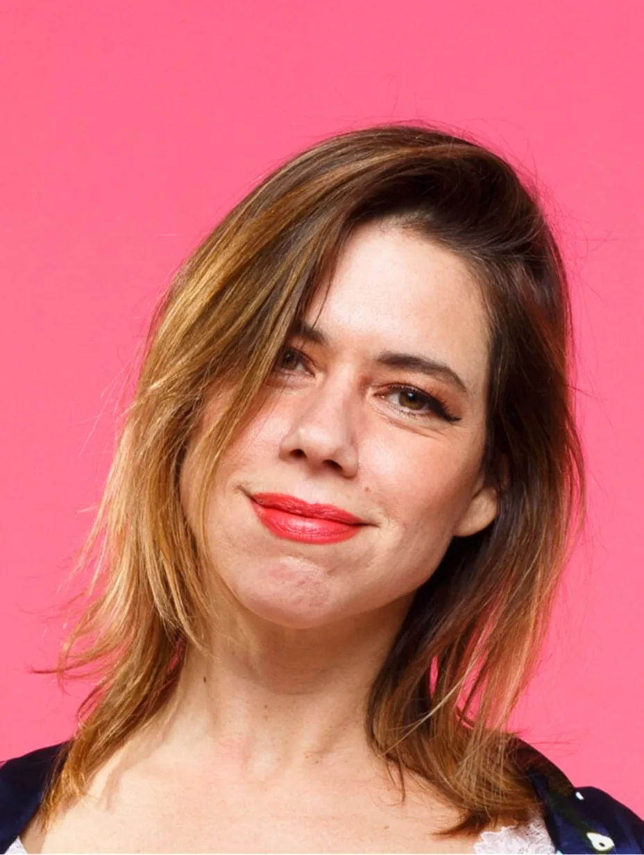 A headshot of English stand up comedian Lou Sanders against a vibrant pink background. A London based comedian known for her unique humor who does comedy shows london
