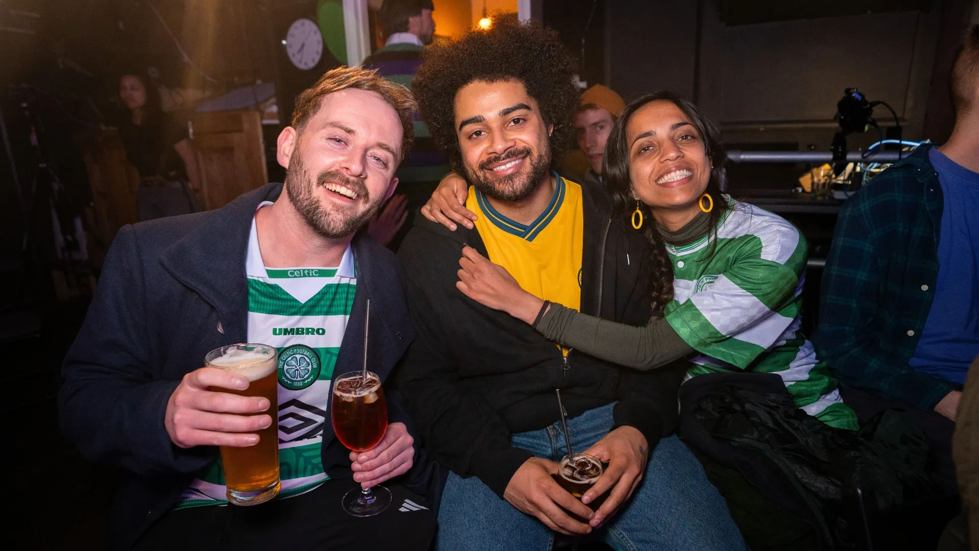 Three smiling audience members, enjoying drinks and posing together, capturing the fun, party atmosphere and strong community at a Comedy Freaks live stand up show in London.