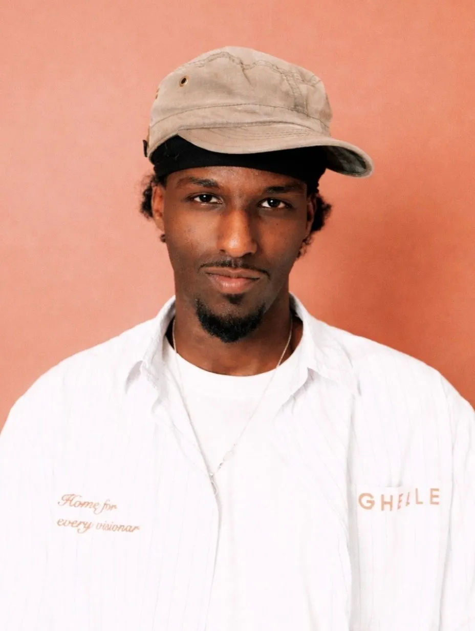 Bamph, a comedian, smiles for a professional headshot photo. Behind him is a light salmon background. 
