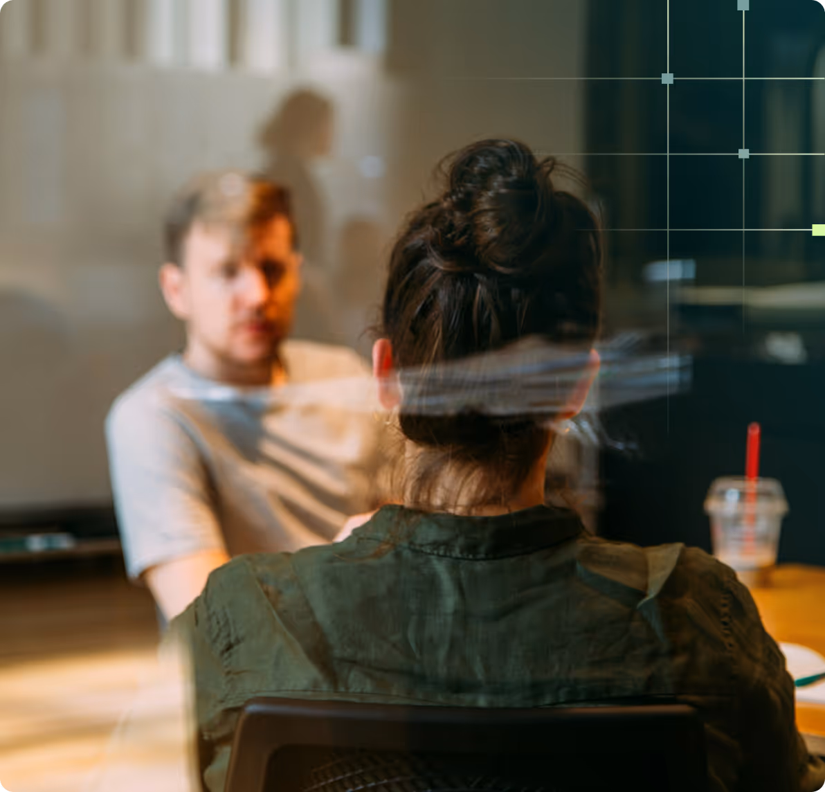 Två personer sitter mitt emot varandra och samtalar vid ett bord i ett mötesrum.