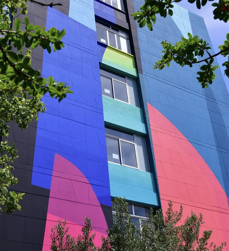 Mur d’immeuble recouvert d’une fresque géométrique aux couleurs vives.