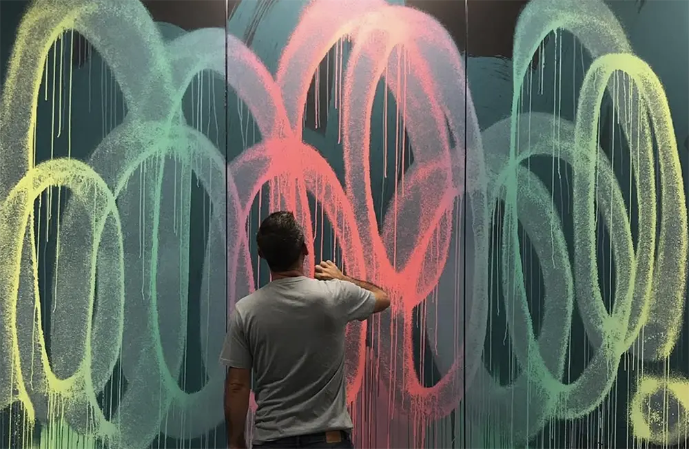 Artiste en train de peindre des boucles colorées sur une grande surface murale.