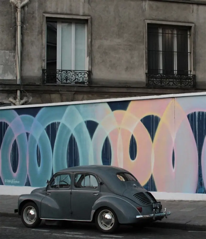 Fresque murale abstraite avec des arcs colorés entrelacés, en arrière-plan d'une voiture ancienne.