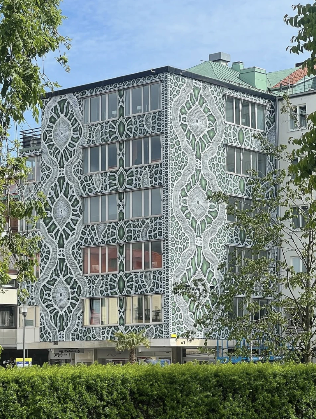 Fresque sur fond vert de style broderie, avec des formes ondulées remplies de verts plus foncés.