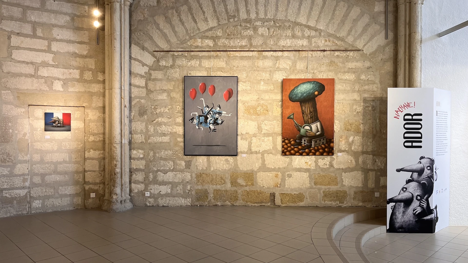 Un mur vouté et des oeuvres accrochées aux murs, le paravent de l'artiste à droite de l'image.
