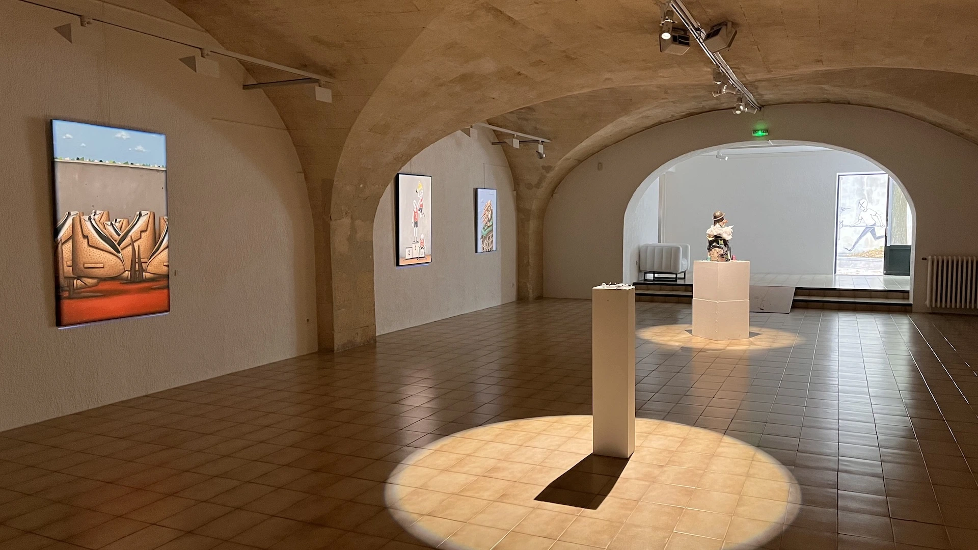 Vue d'ensemble de la seconde pièce voutée de l'espace, pupitres au milieu et oeuvres accrochées aux murs.
