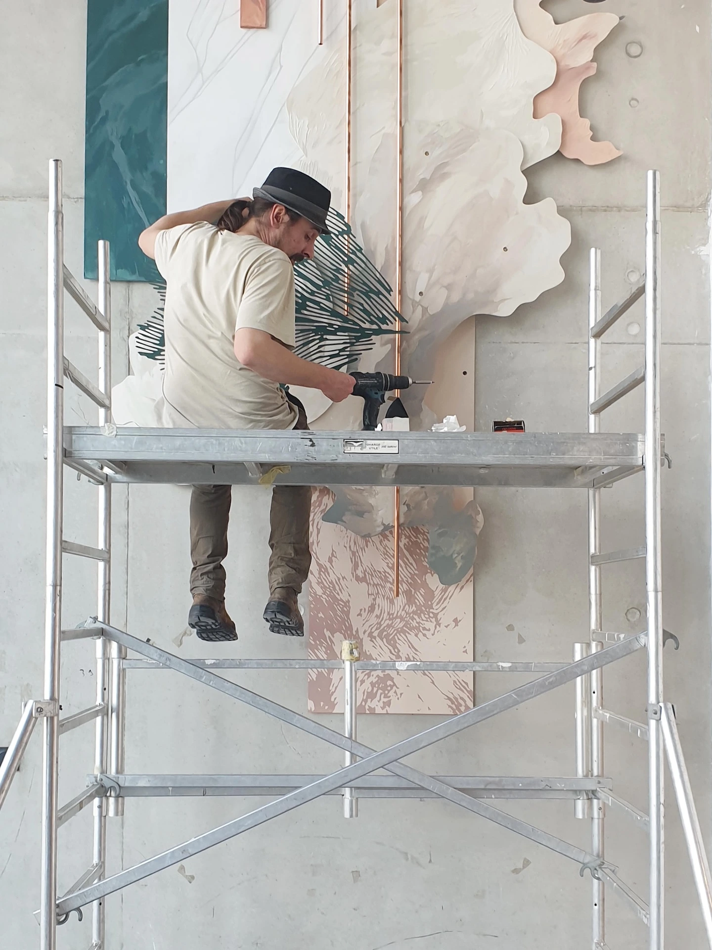 Photo d'un homme assis sur un échafaudage entrain d'accrocher les éléments de l'oeuvre.