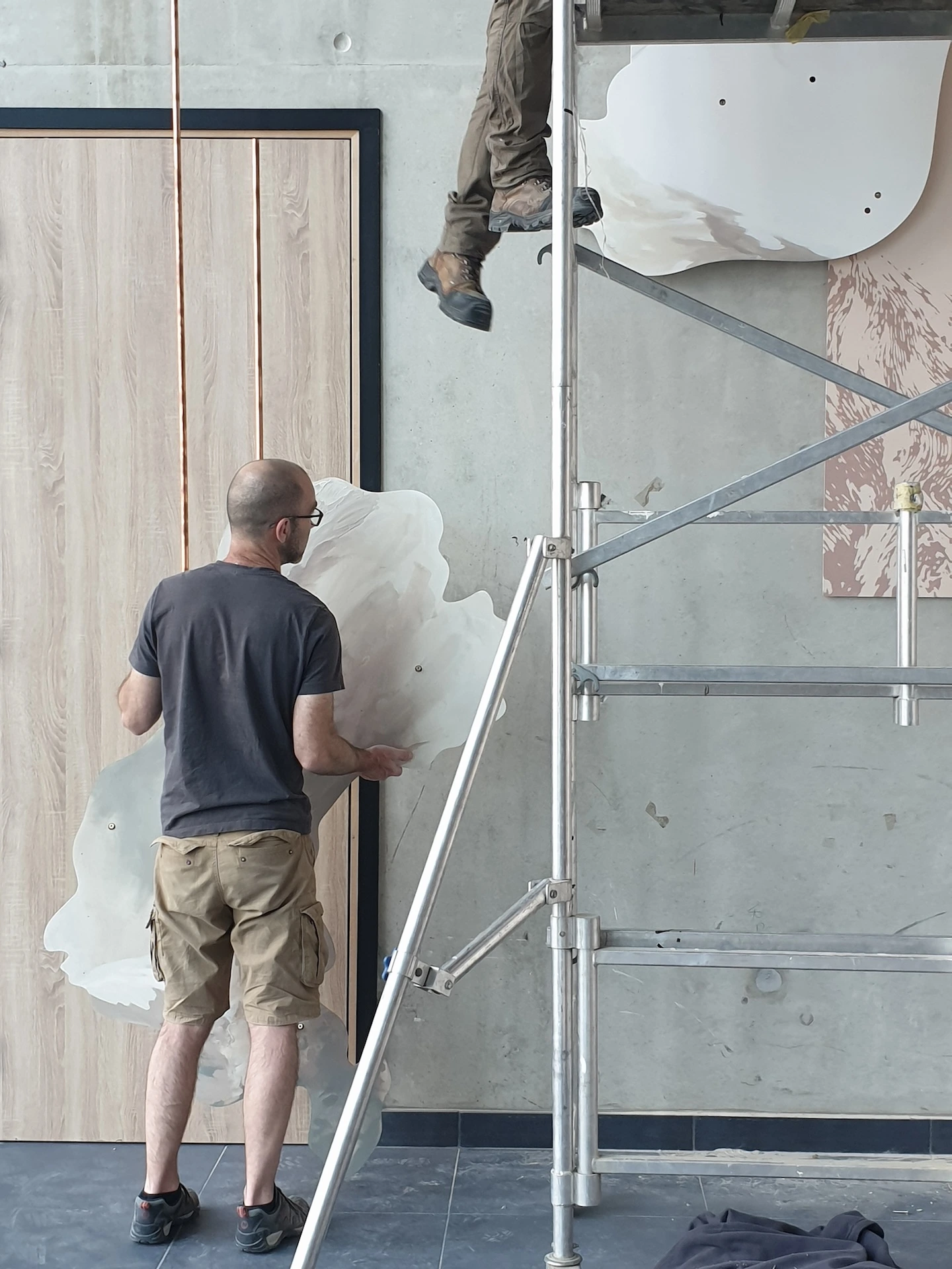 Photo d'un homme debout, à côté d'un échafaudage, un élément de l'oeuvre à la main.