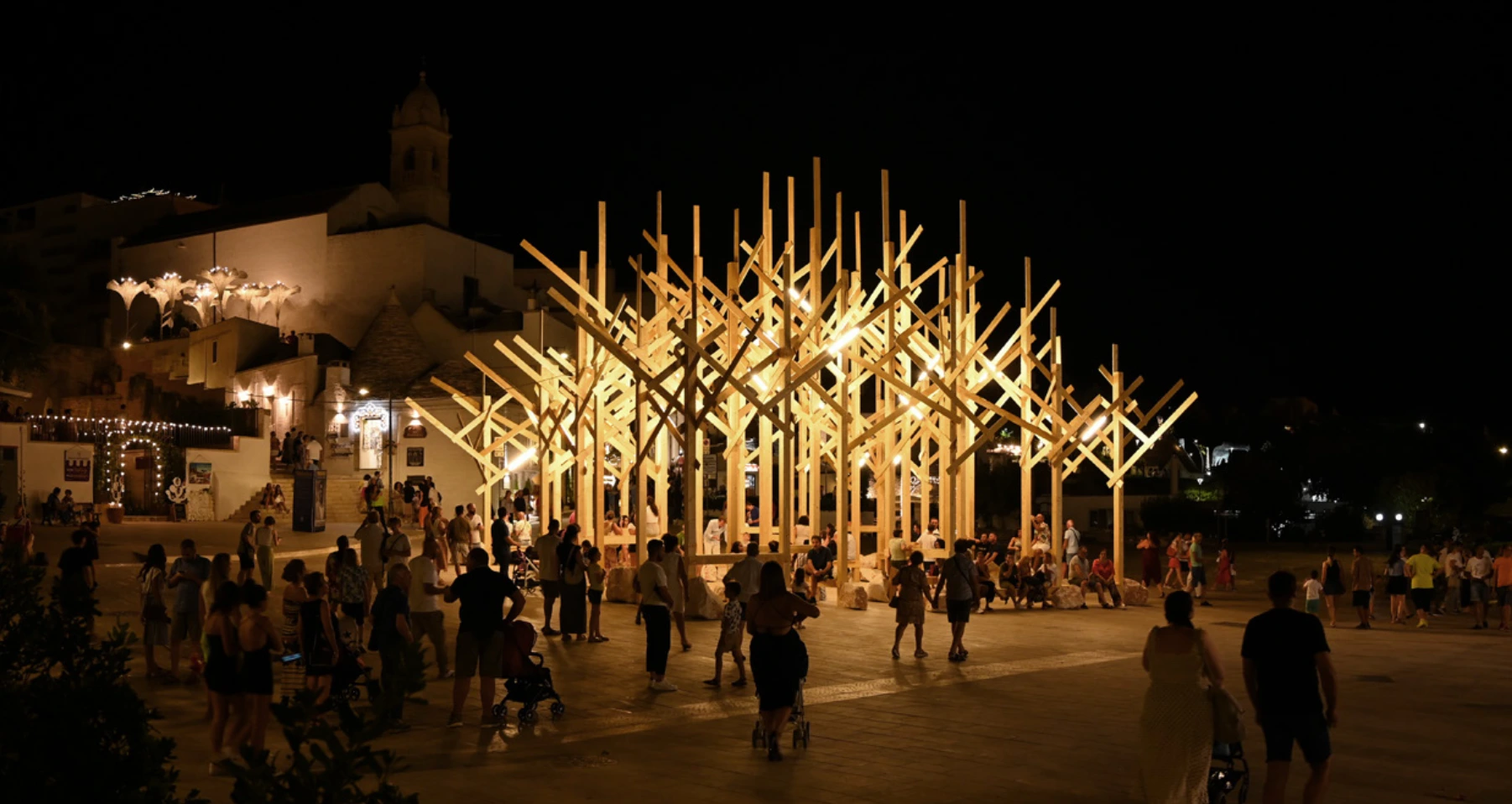 Installation lumineuse en bois en extérieur, de nuit, avec des passants