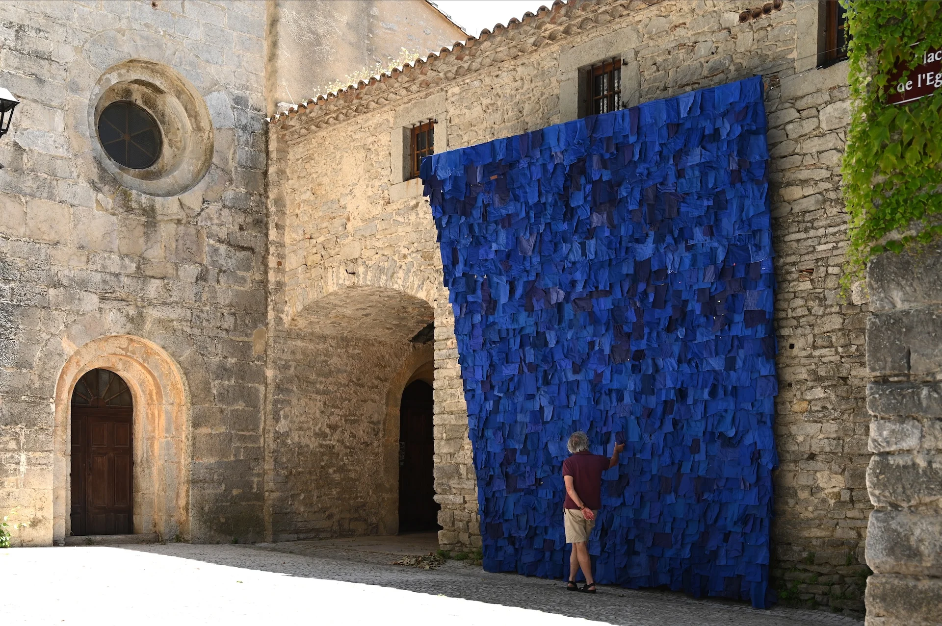 Mur de carrés bleus en tissu ou papier, installé sur une façade en pierre ancienne