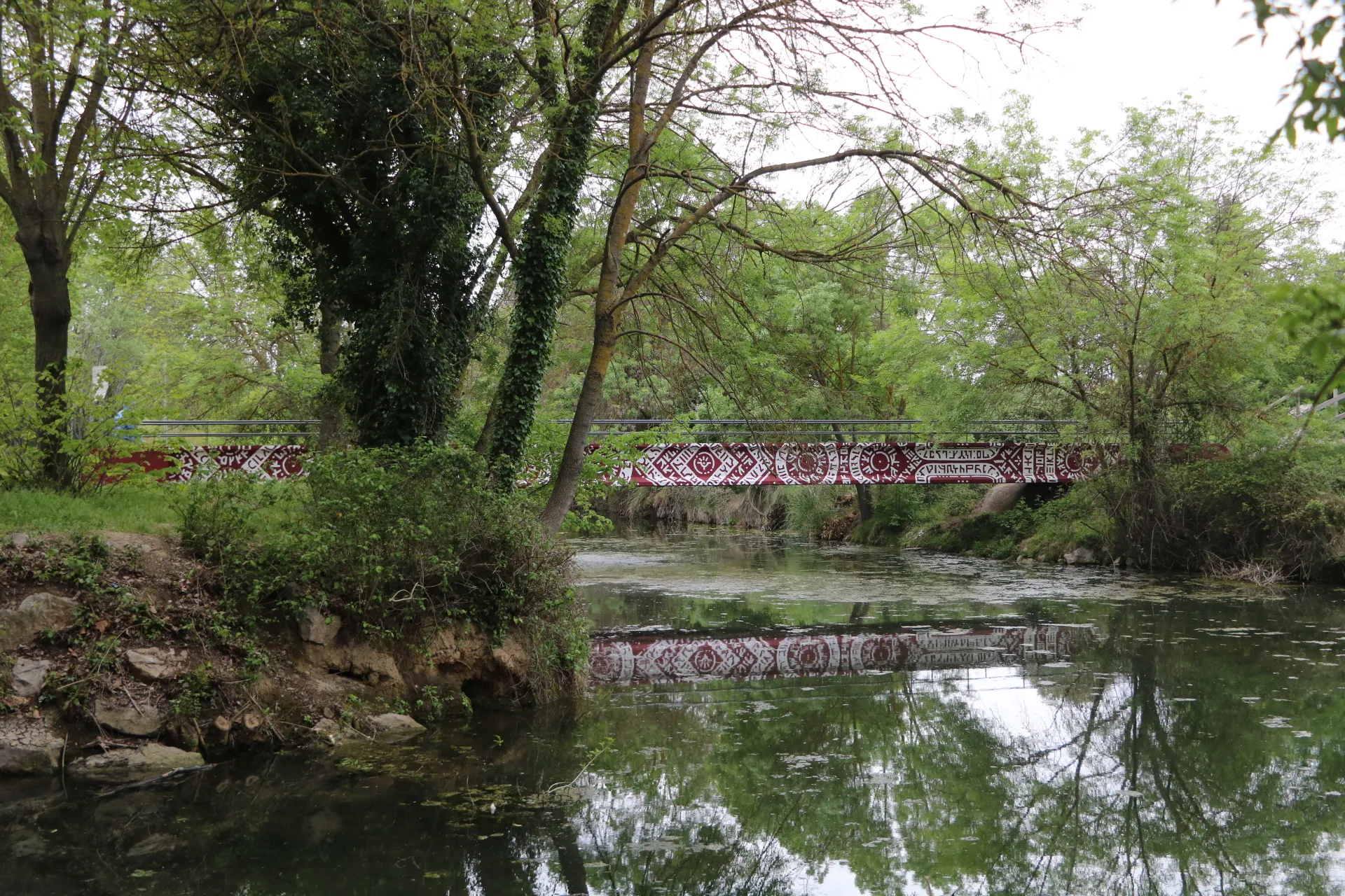 Passerelle décorée reflétée dans l’eau d'une rivière bordée de végétation