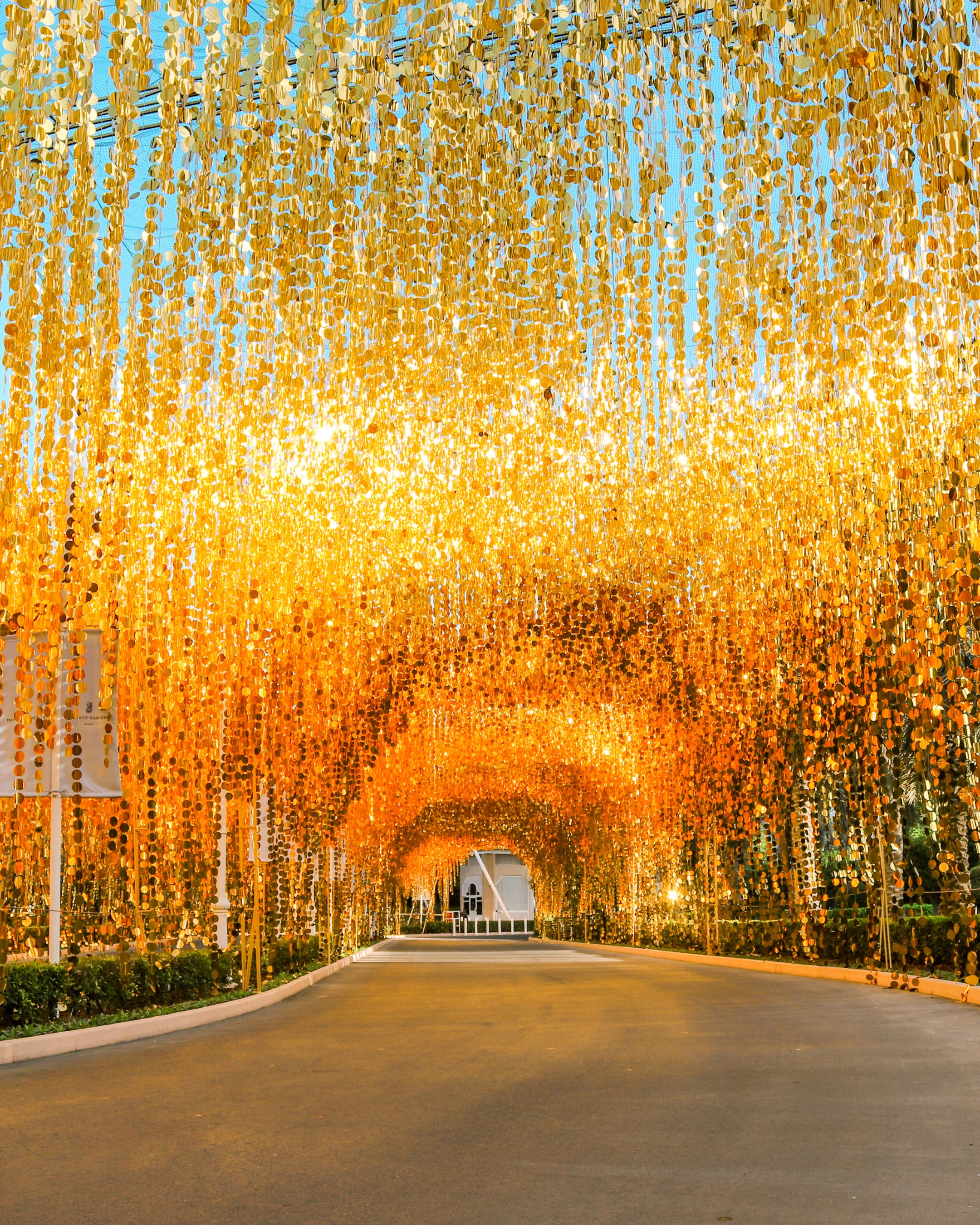 Tunnel lumineux doré formé de rubans suspendus, créant une ambiance chaleureuse au coucher du soleil