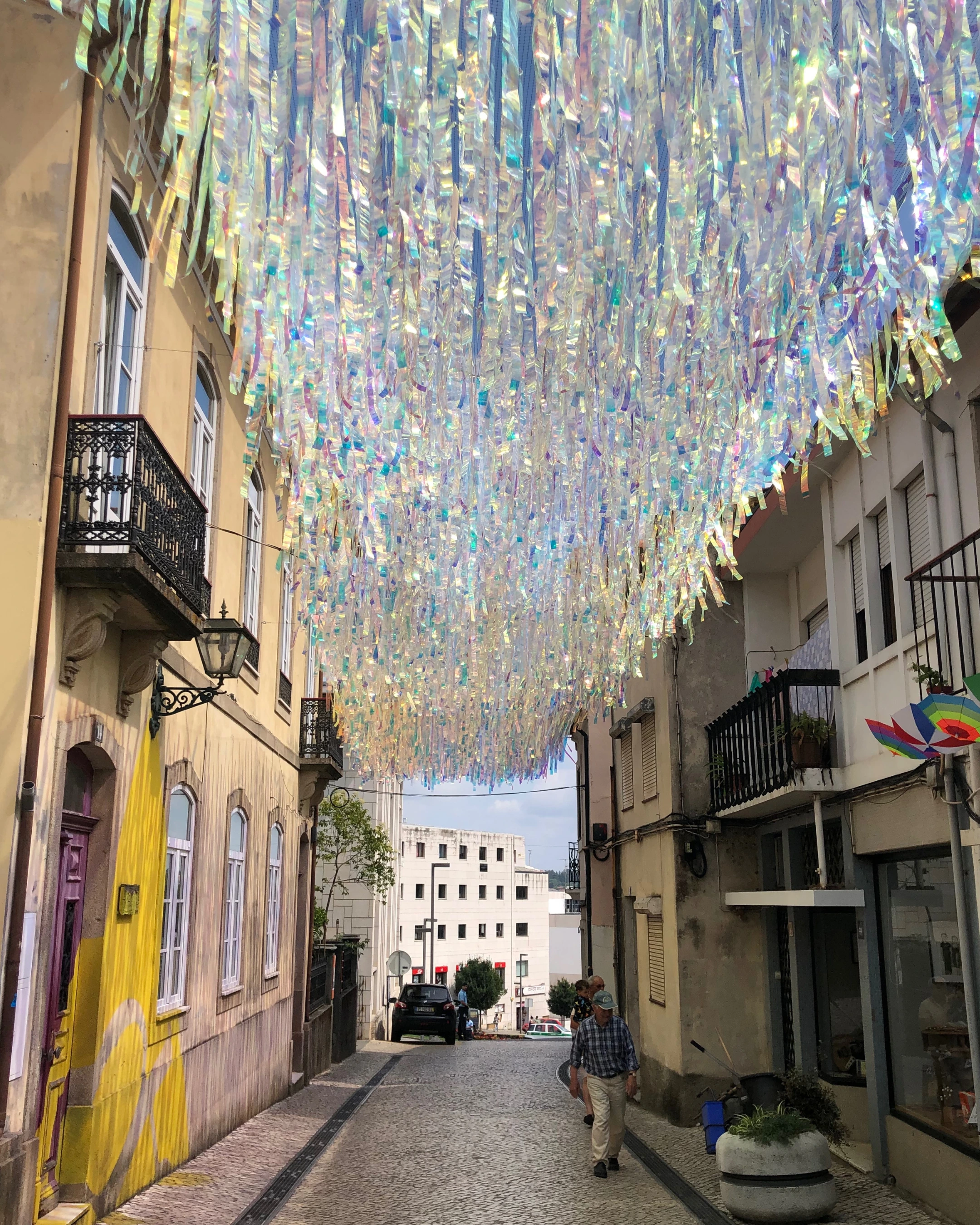 Rue piétonne étroite ornée de centaines de rubans irisés flottant au-dessus des passants