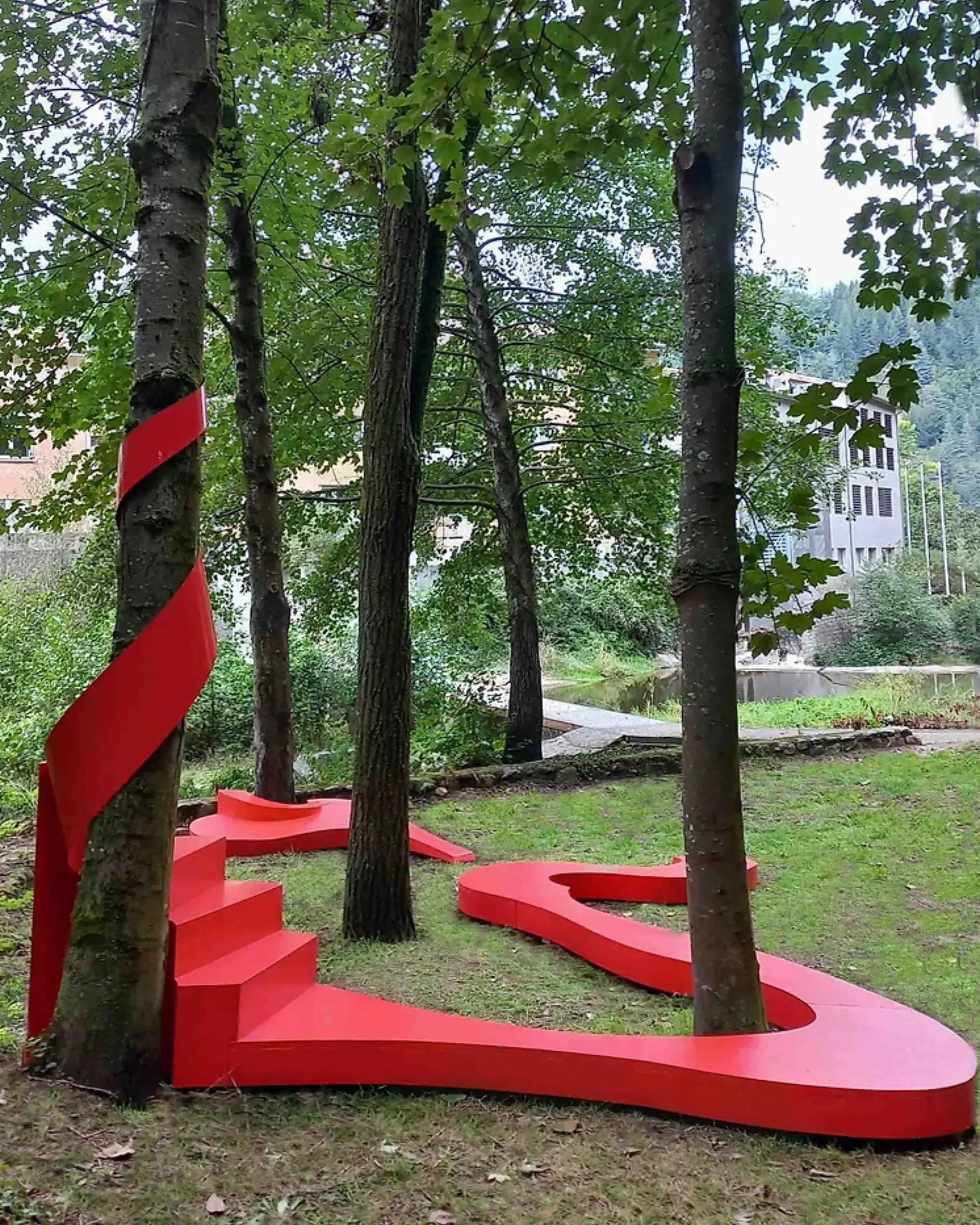 Installation rouge ondulante au sol, épousant les courbes d’arbres dans un espace naturel arboré