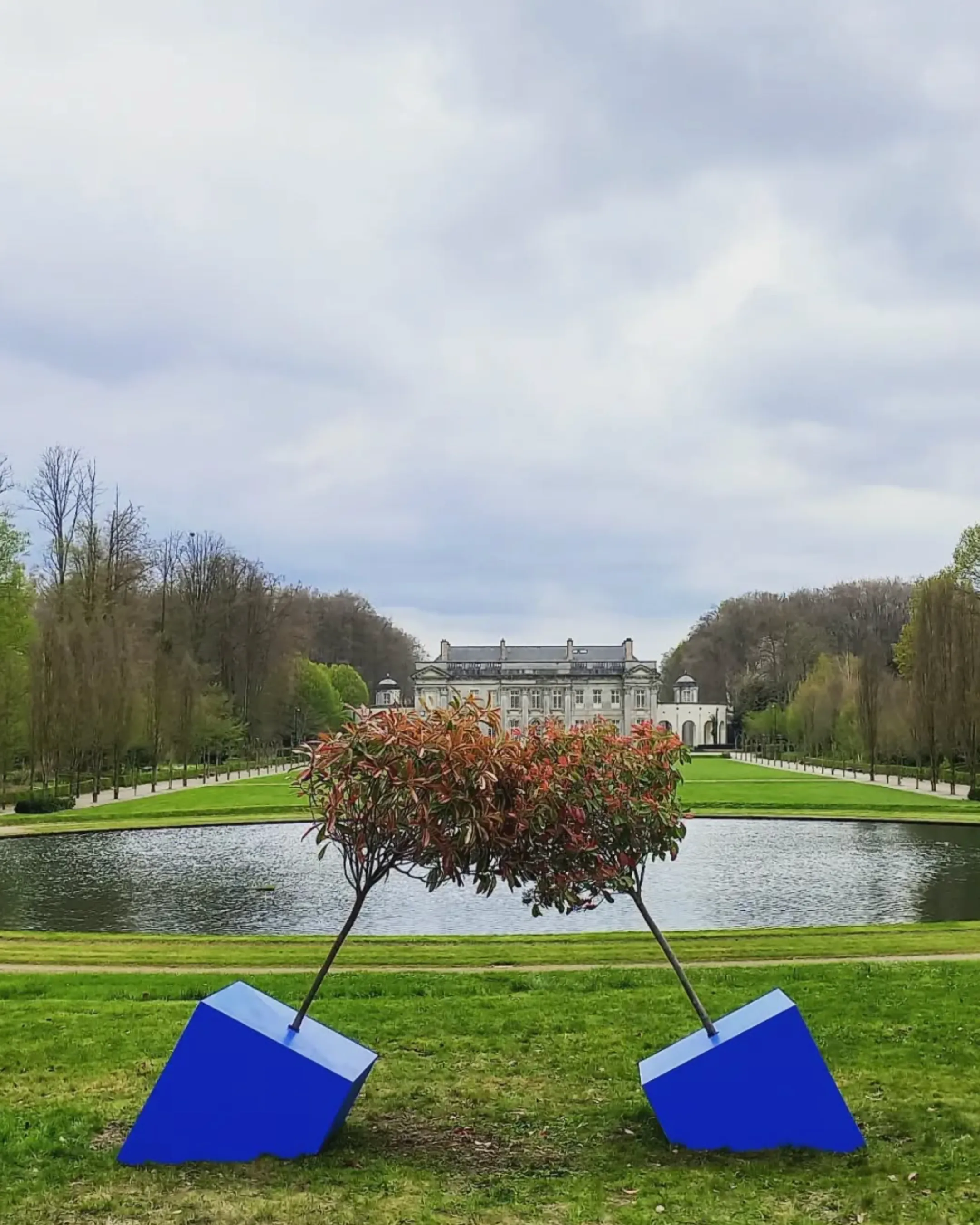 Structure géométrique bleue soutenant un arbuste sphérique au bord d’un bassin symétrique dans un jardin à la française