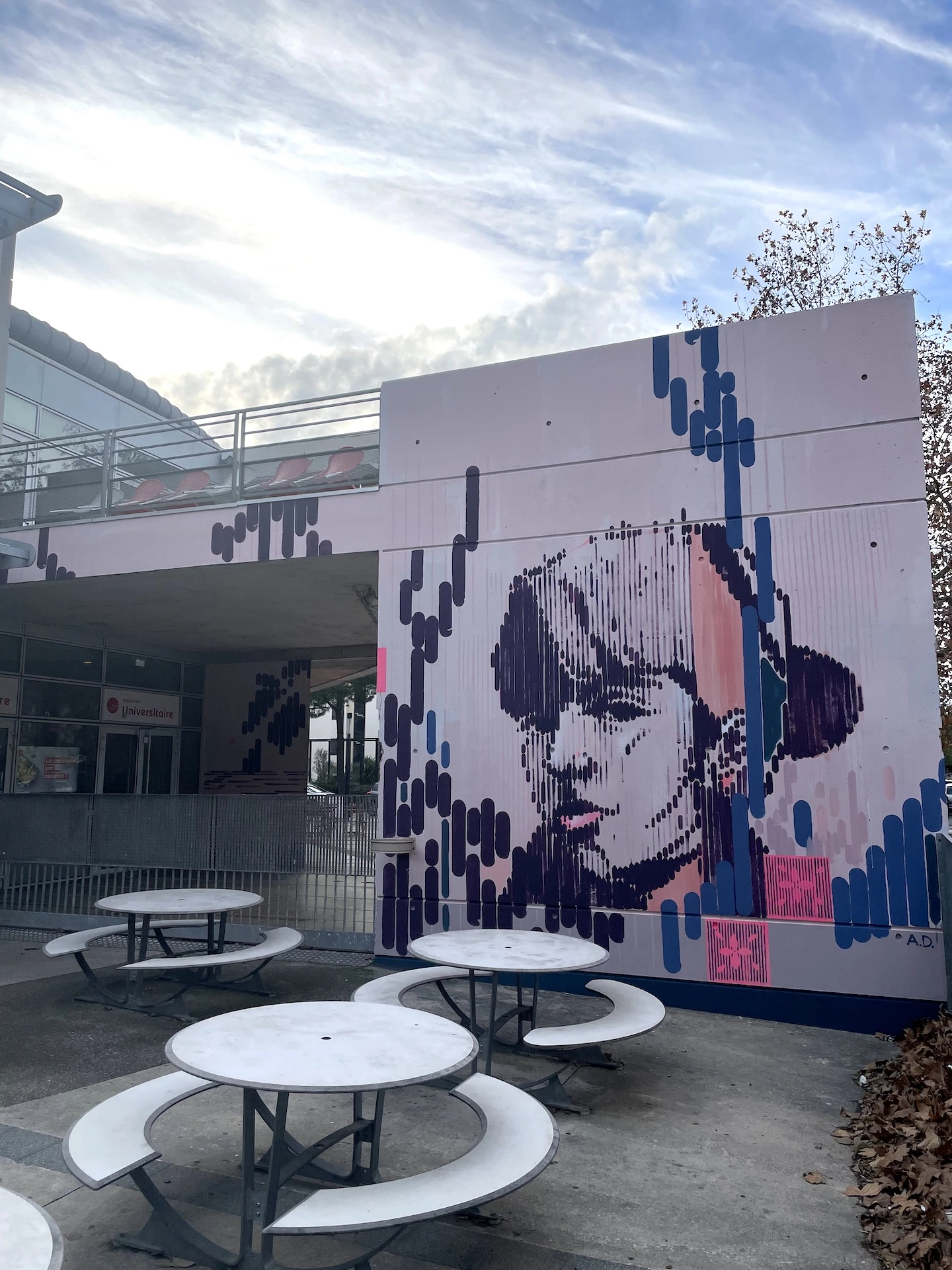 Fresque murale représentant un portrait féminin stylisé entouré de formes graphiques, avec des tables extérieures au premier plan