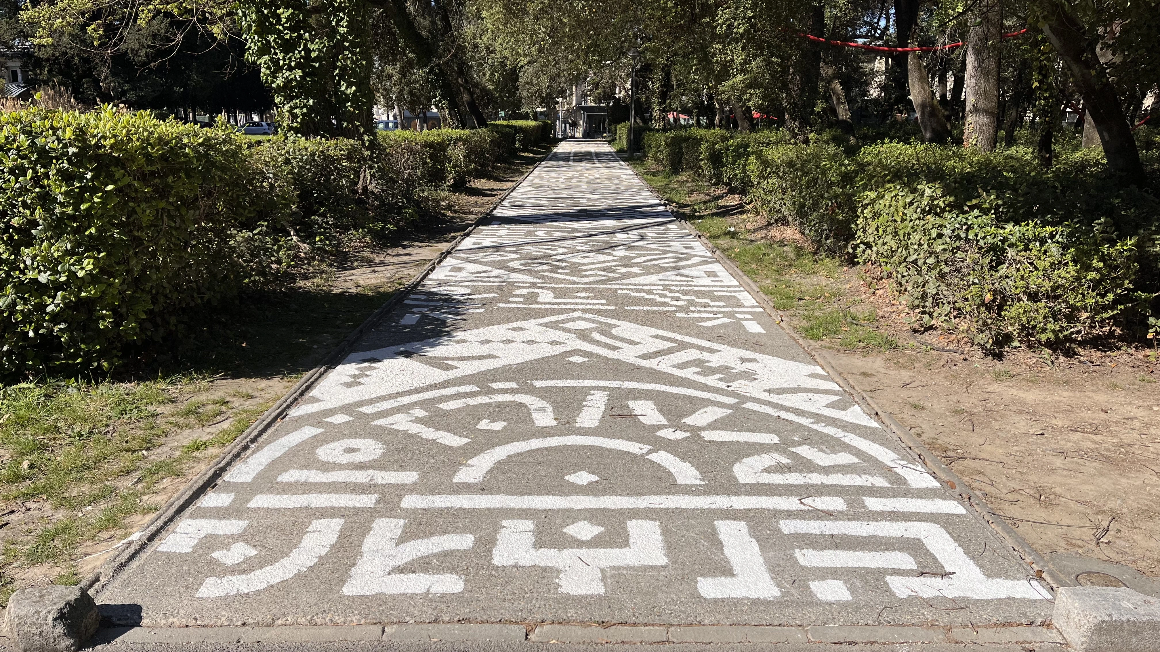 Photo d'une fresque au sol, des symboles blancs jonchent une allée en béton.