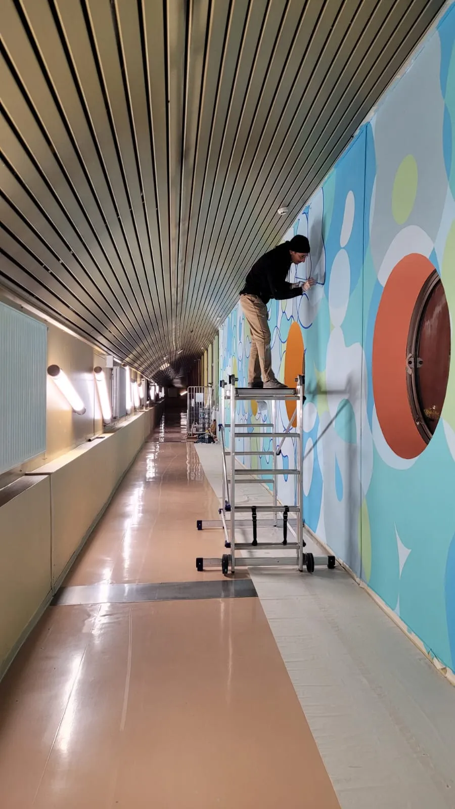 Photo du couloir où l'on voit l'artiste peindre perché sur un échafaudage.