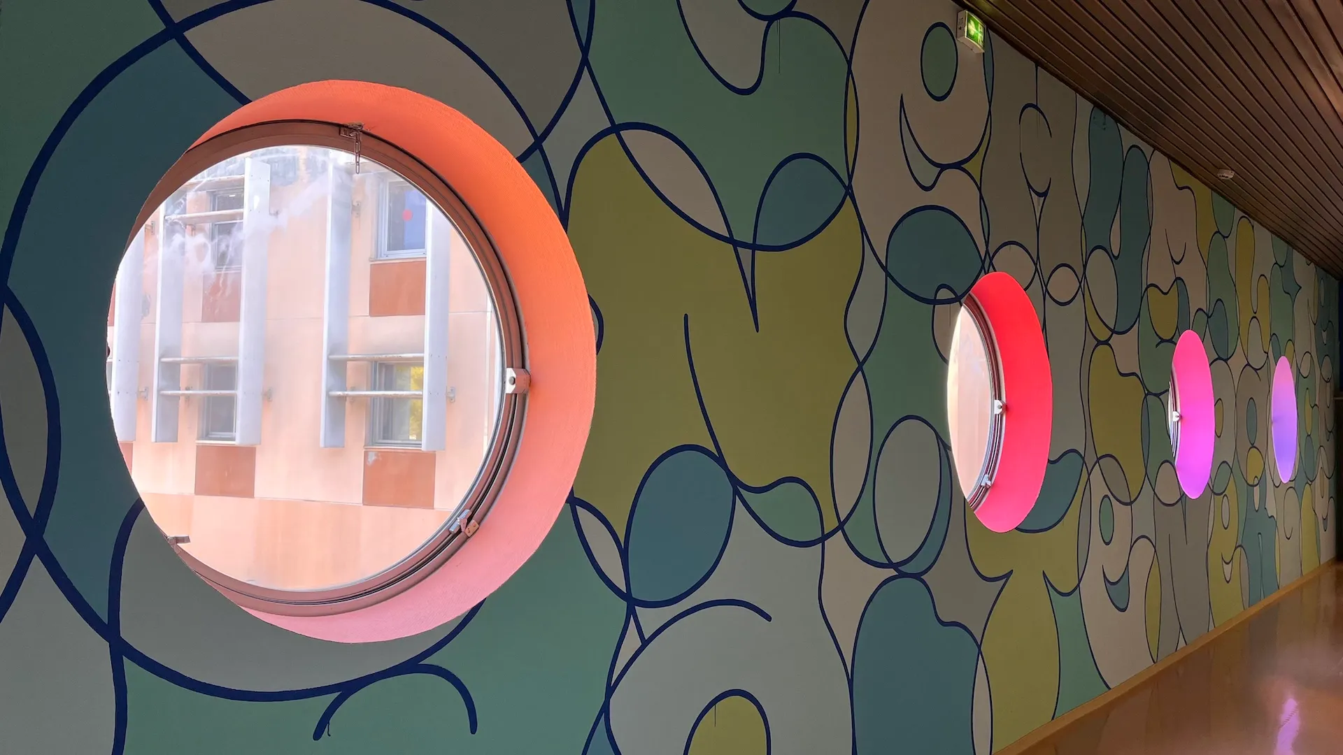 Photo d'un couloir avec des fenêtres en hublot, dont le mur est recouvert d'une fresque aux tons bleu clair.
