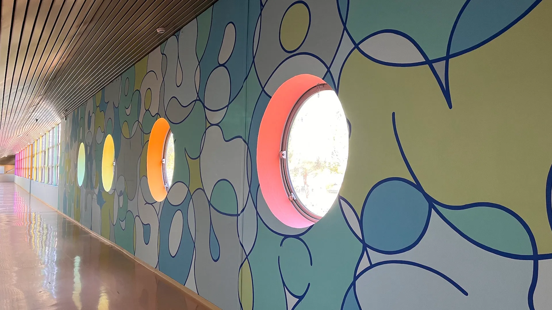 Photo d'un couloir avec des fenêtres en hublot, dont le mur est recouvert d'une fresque aux tons bleu clair.