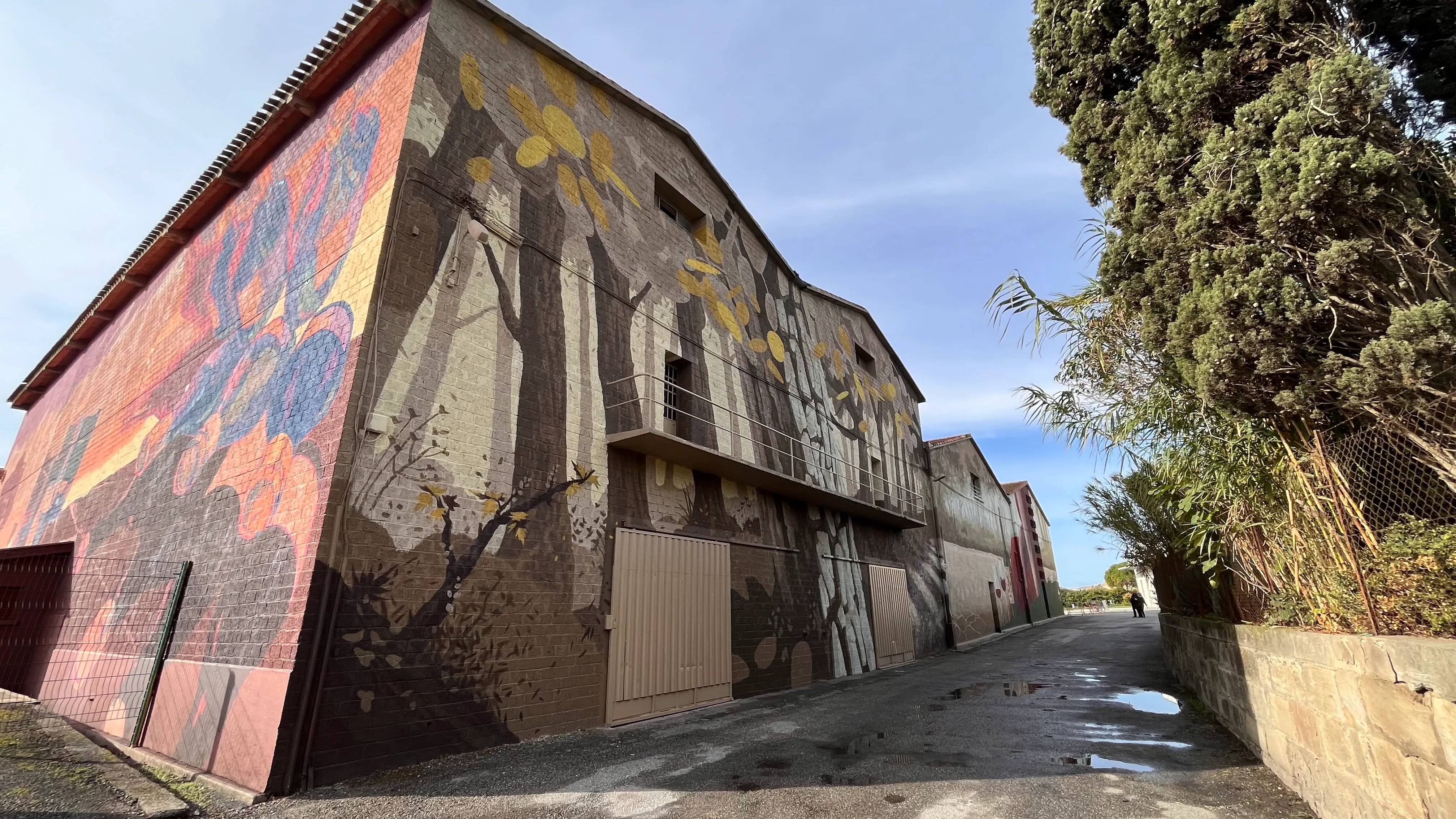 Fresque murale en cours de réalisation sur un entrepôt, avec des échafaudages visibles.