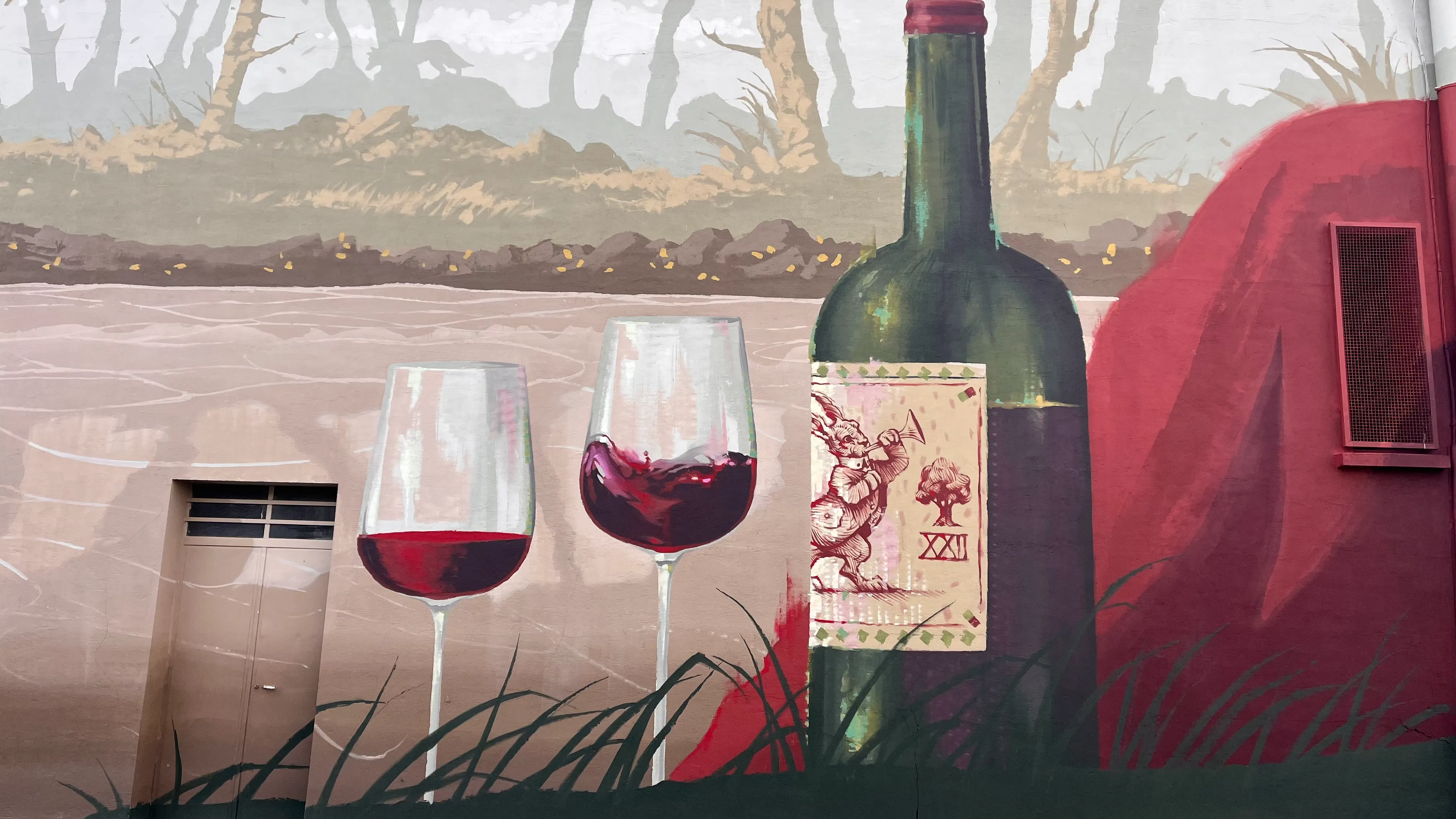 Détail de fresque représentant des verres de vin rouge et une bouteille dans un paysage stylisé.