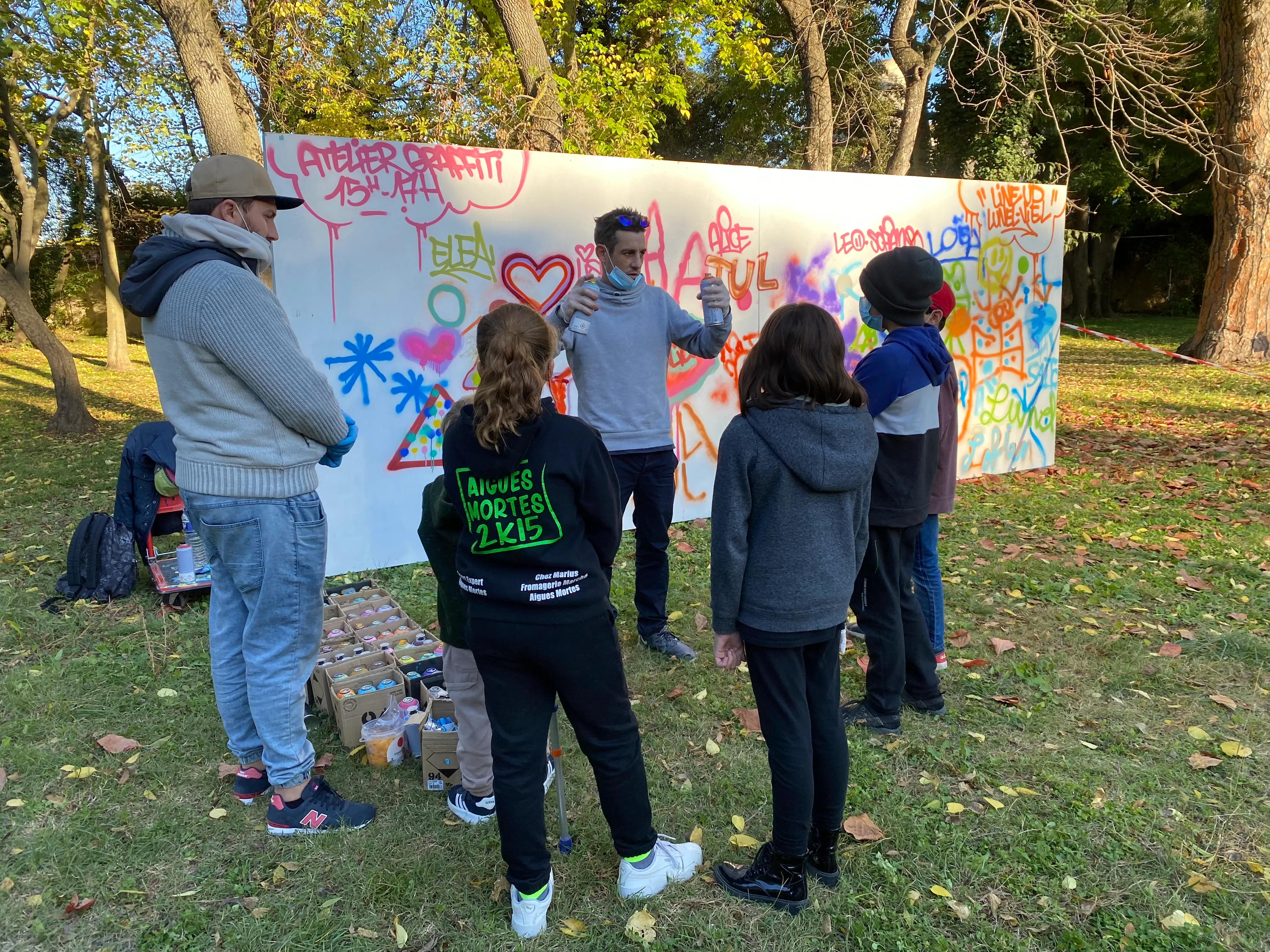 Atelier de médiation artistique en plein air avec des jeunes devant un mur d'expression.