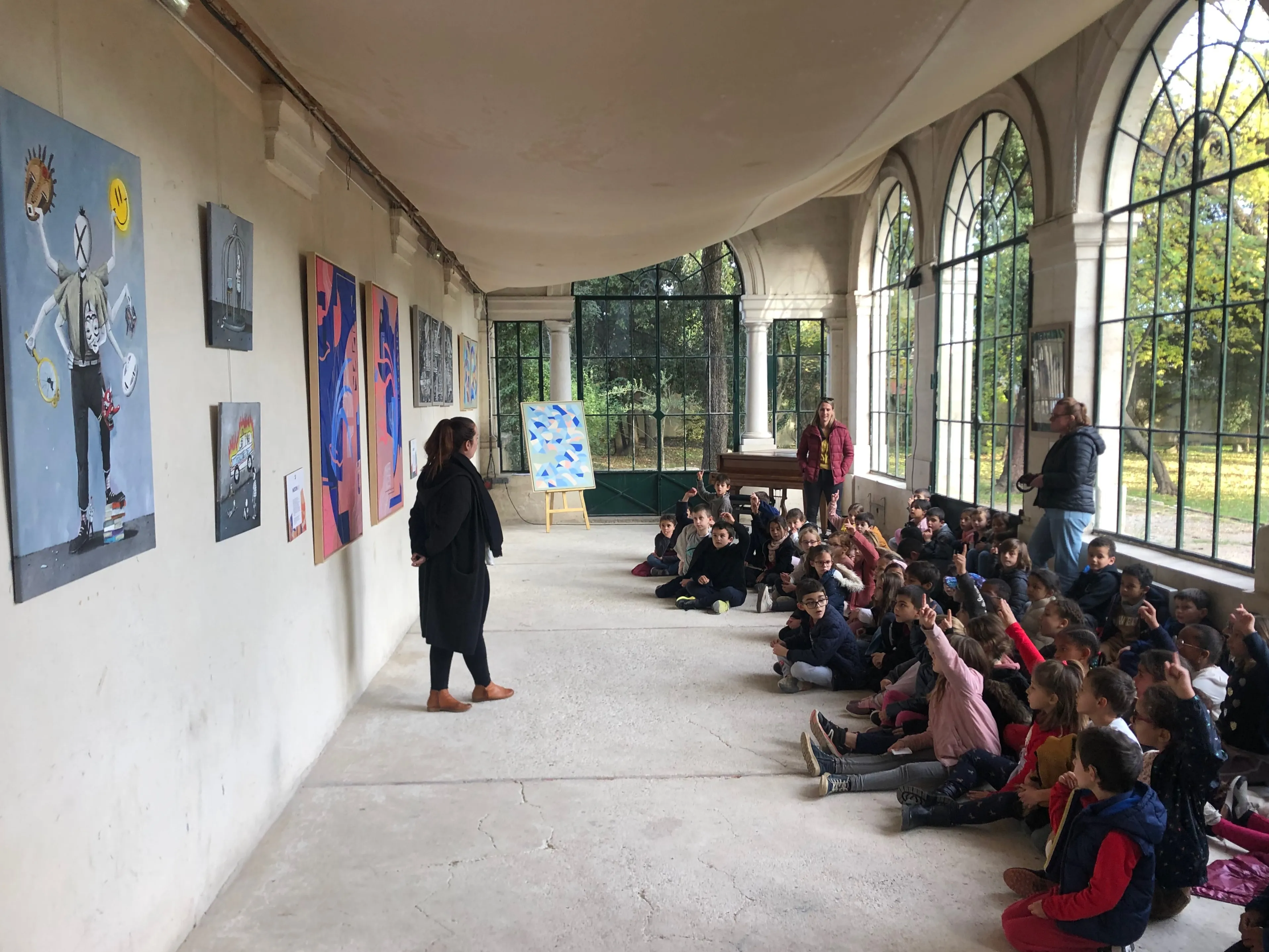 Groupe d'enfants assis devant une série d'œuvres exposées dans une galerie lumineuse.