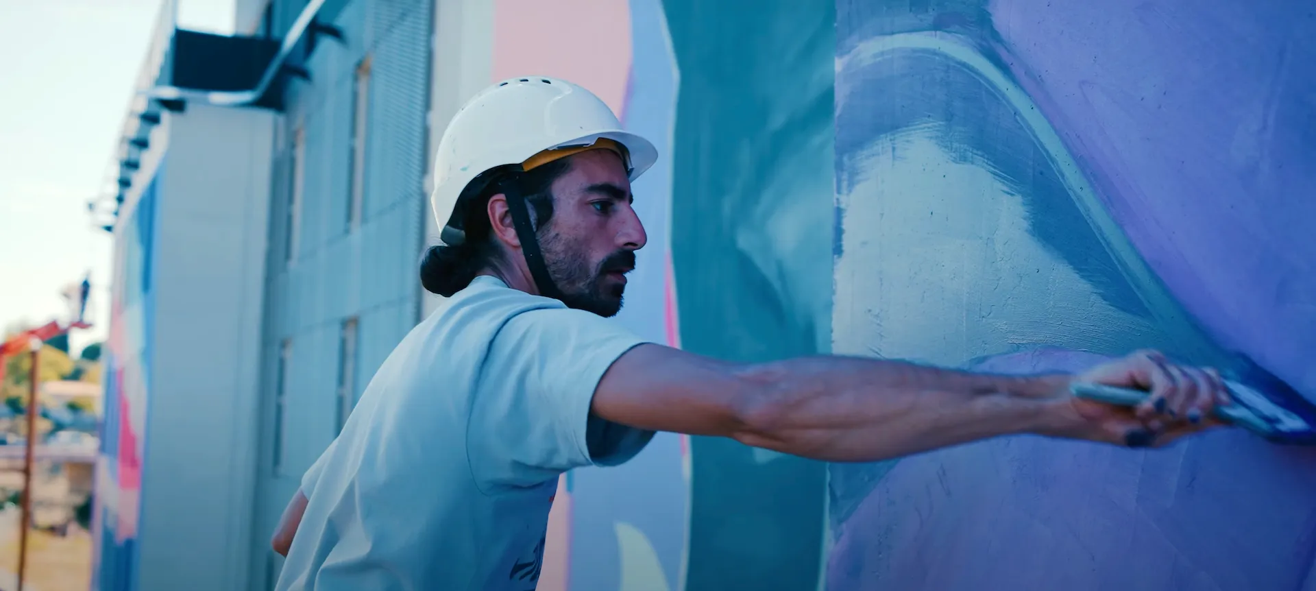 L'artiste Enaer peignant à main levée des formes ondulées sur un mur bleu.