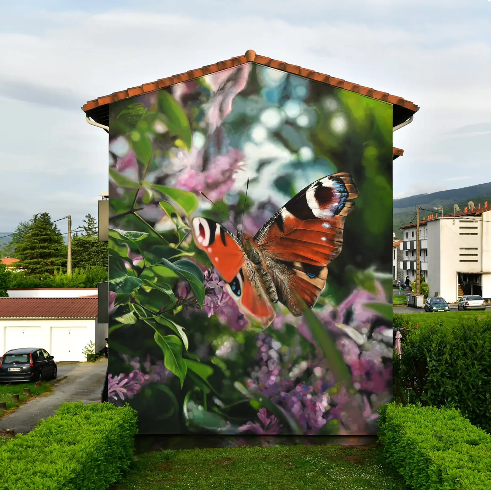 Fresque colorée représentant un papillon et une plante sur la façade d’un petit immeuble en milieu urbain.