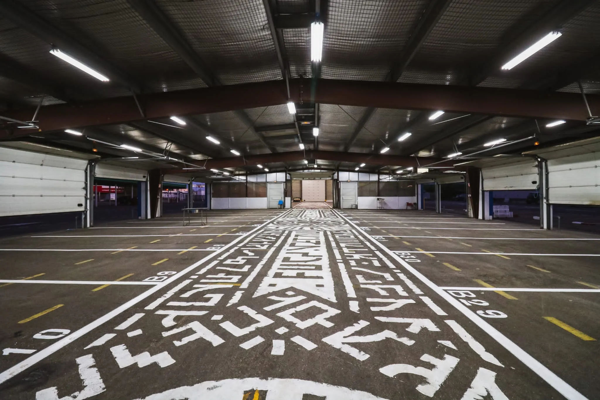 Perspective centrale d’un parking dont le sol est recouvert de motifs graphiques blancs sur fond noir.