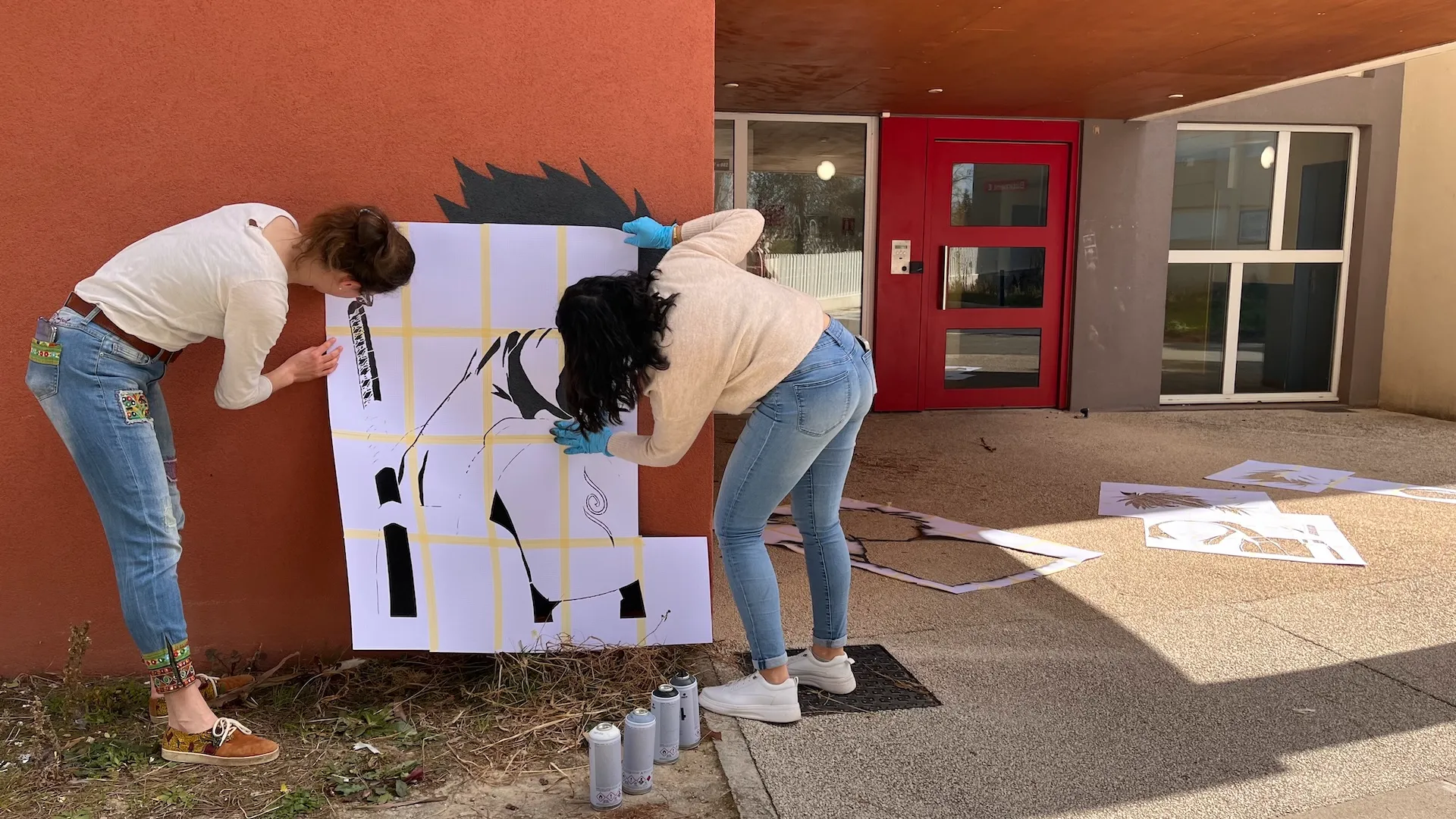 Photo de deux jeunes filles réalisant un pochoir sur un mur orange.