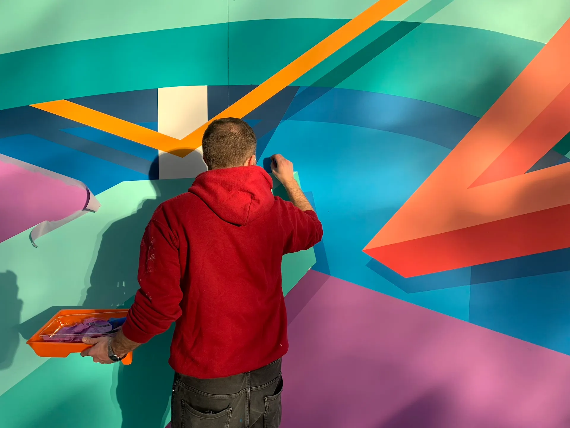 Vue rapprochée d’un artiste peignant une fresque abstraite aux formes géométriques et couleurs vives.