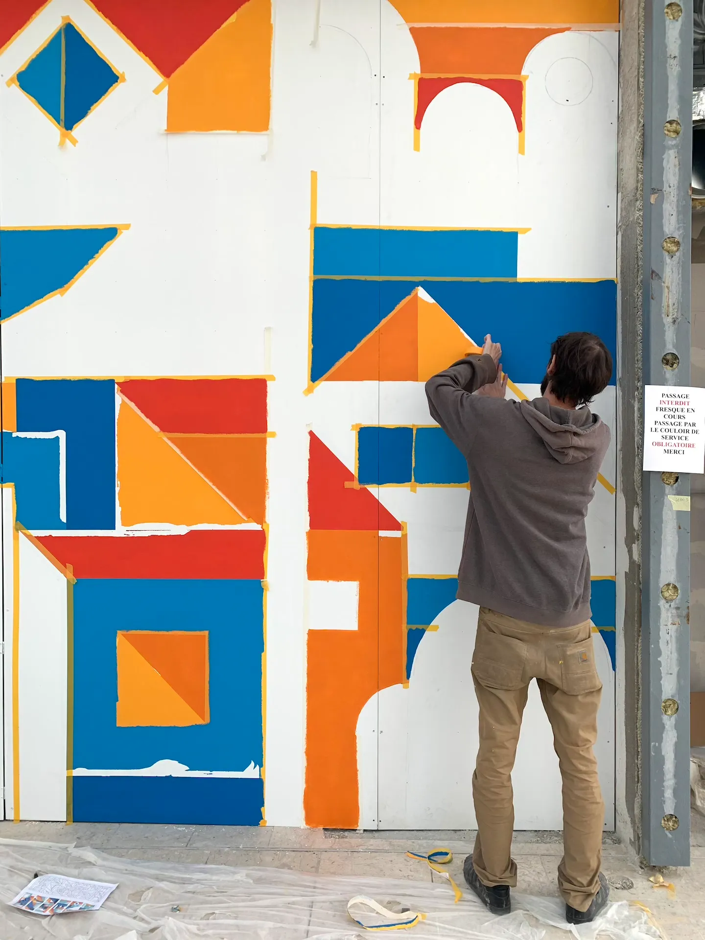 Artiste peignant une fresque géométrique colorée sur un mur blanc.