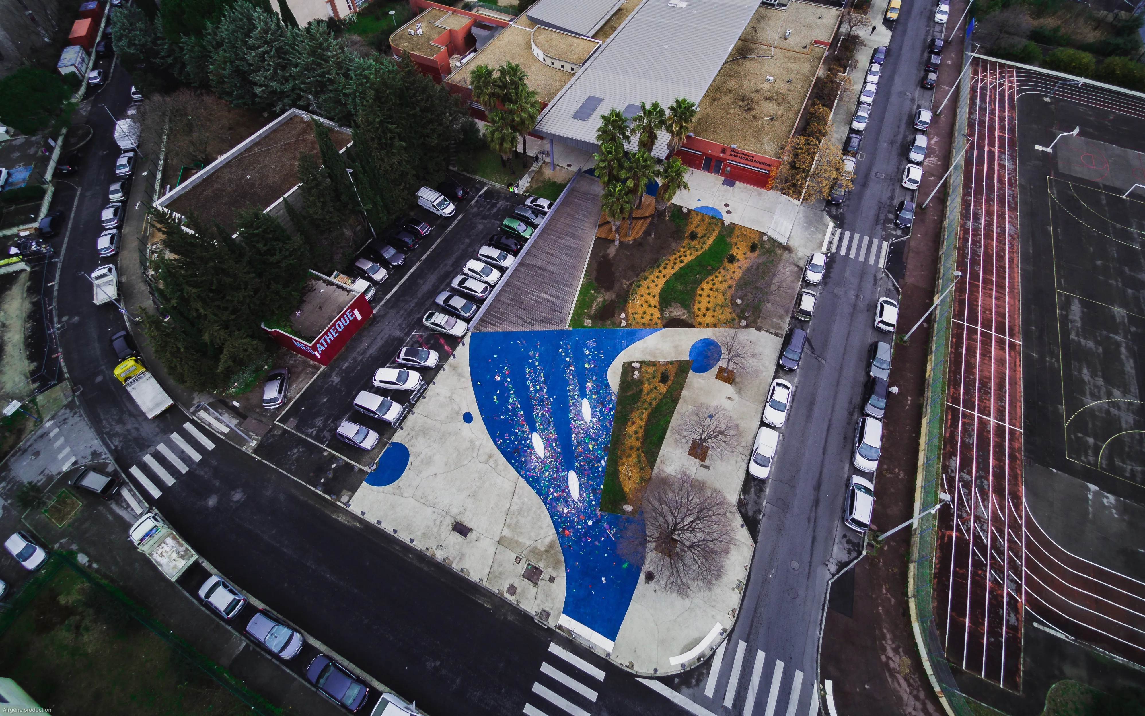Vue aérienne d'un parvis peint en bleu comme si c'était une mer, on voit les rues adjacentes.