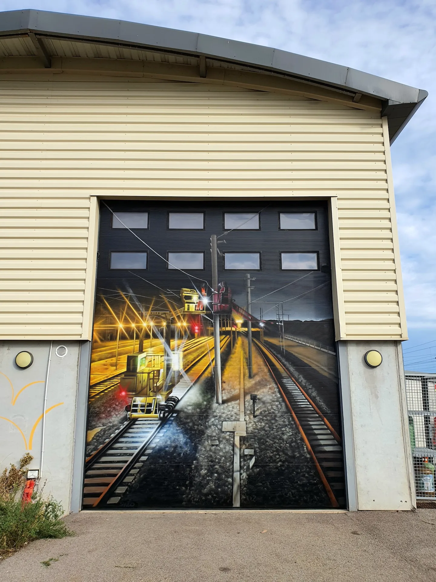Porte de hangar peinte en trompe-l’œil montrant un tramway lancé sur des rails, vue frontale avec effet de profondeur