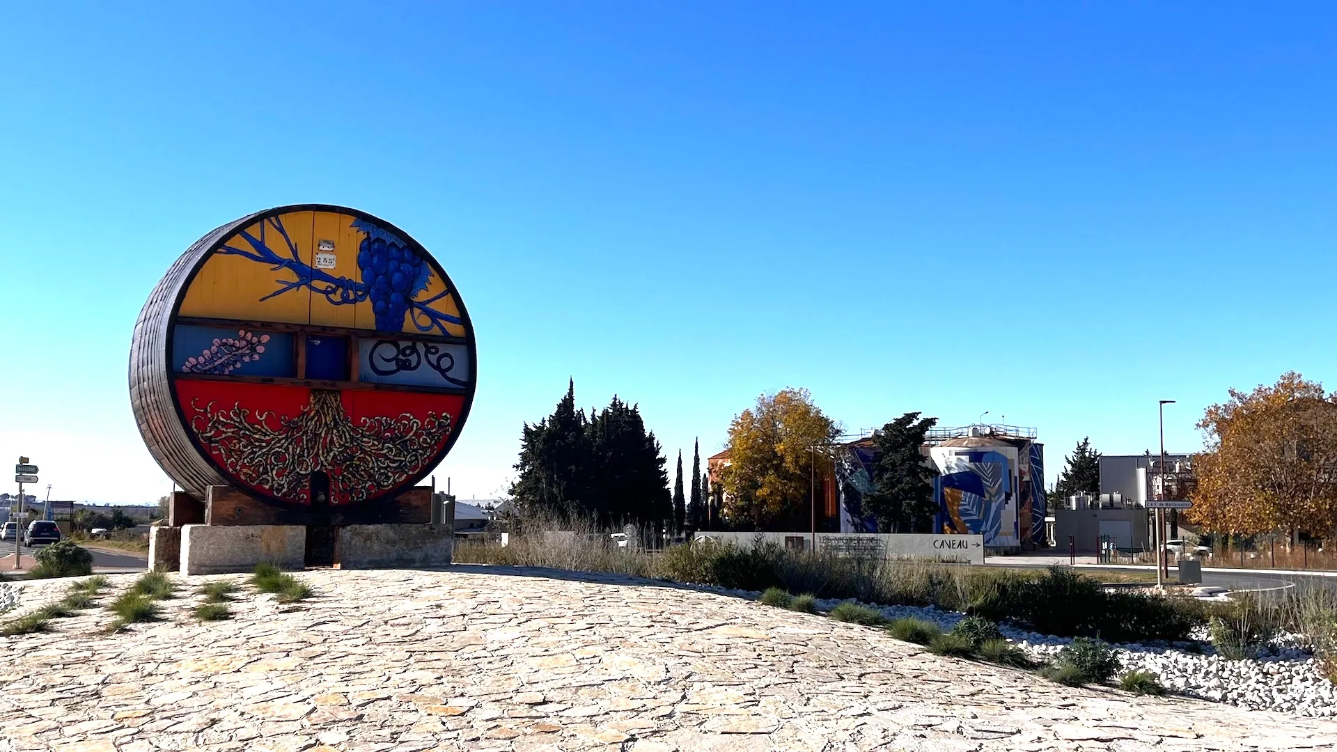 Installation artistique circulaire peinte, visible dans un paysage ouvert mêlant éléments naturels et aménagements urbains