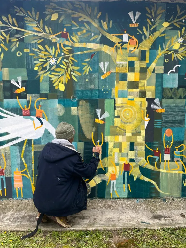 Artiste en train de peindre une fresque murale aux formes végétales stylisées et aux couleurs vertes et jaunes