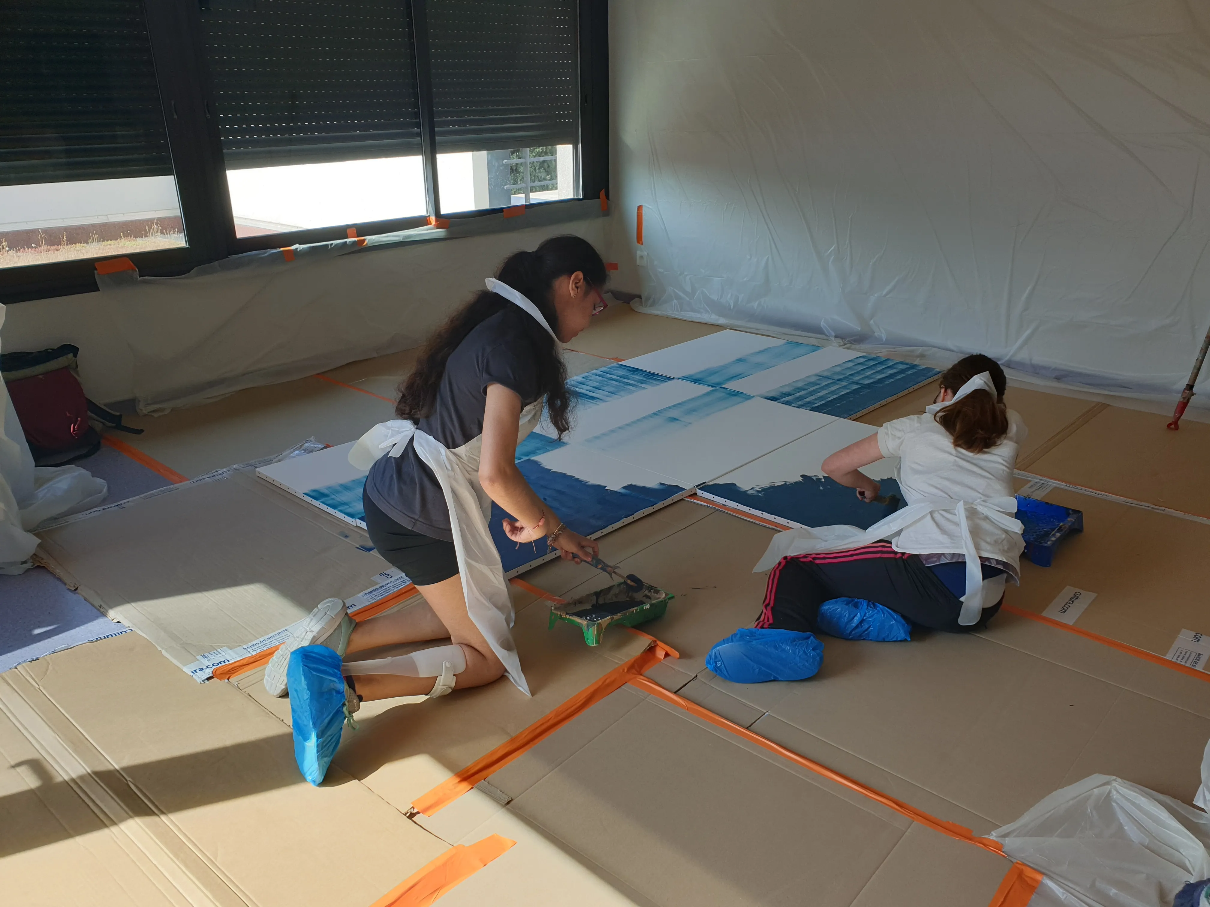 Atelier de création artistique en intérieur, avec plusieurs personnes travaillant au sol sur une composition peinte