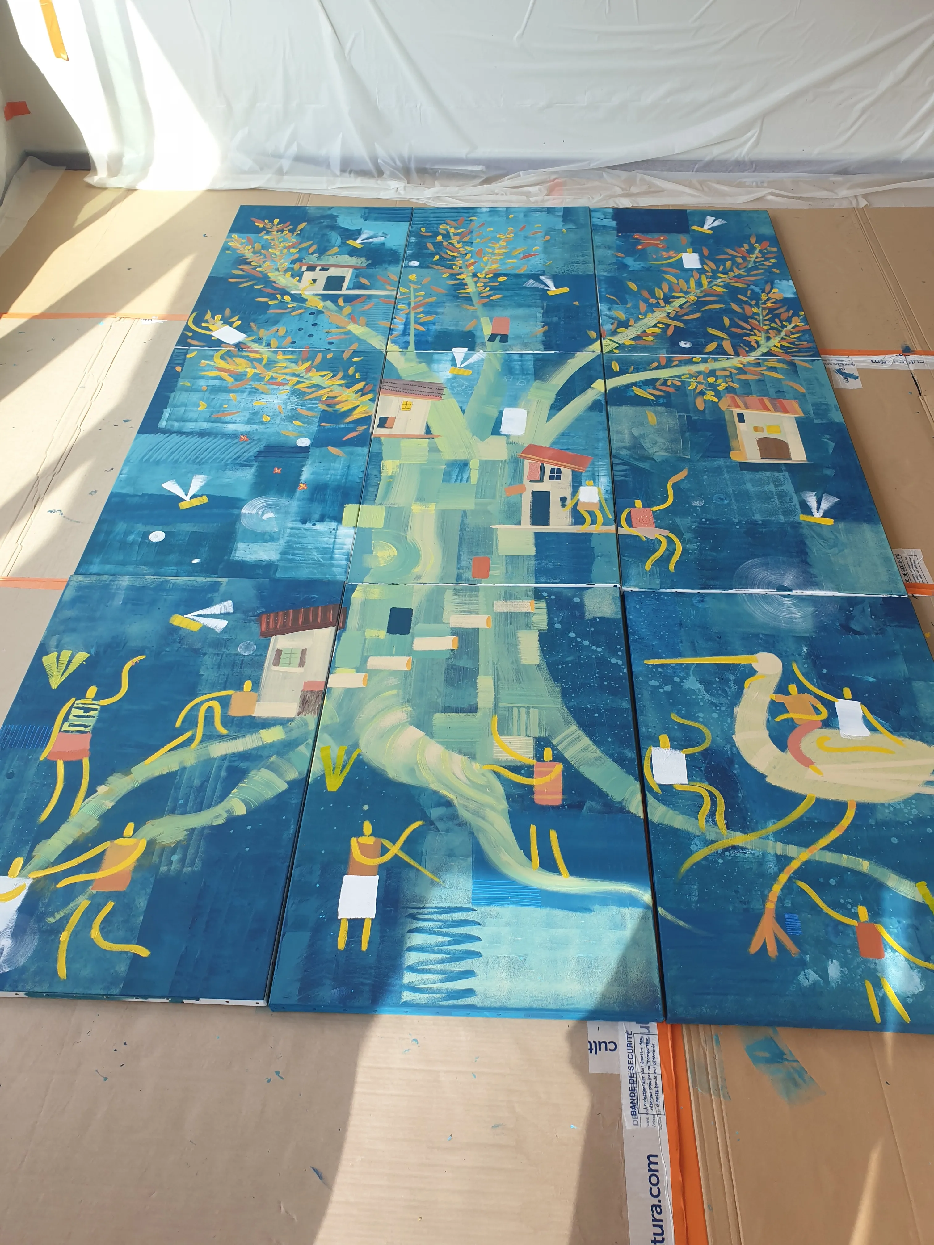 Vue plongeante sur une peinture en cours de réalisation, aux motifs abstraits bleus et verts, posée au sol